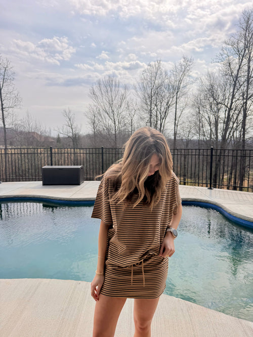 Woman standing by a pool wearing a brown dress with a striped set.