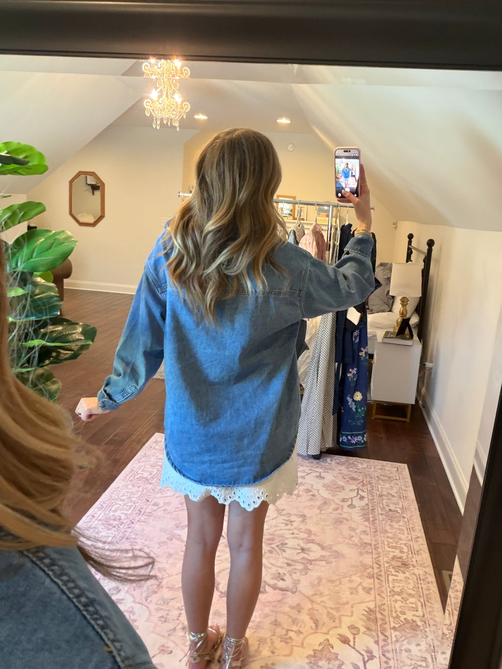Woman taking a mirror selfie wearing a denim shirt and white lace shorts in a store.