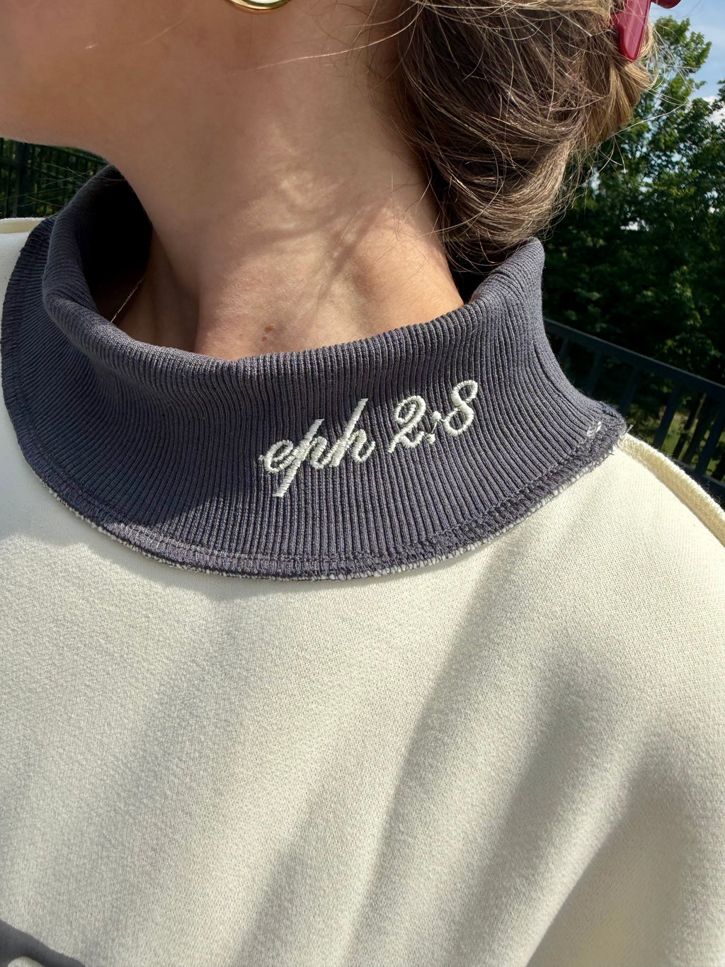 Person wearing a garment with 'eph 2:8' embroidered on a dark collar against a blurred natural background.