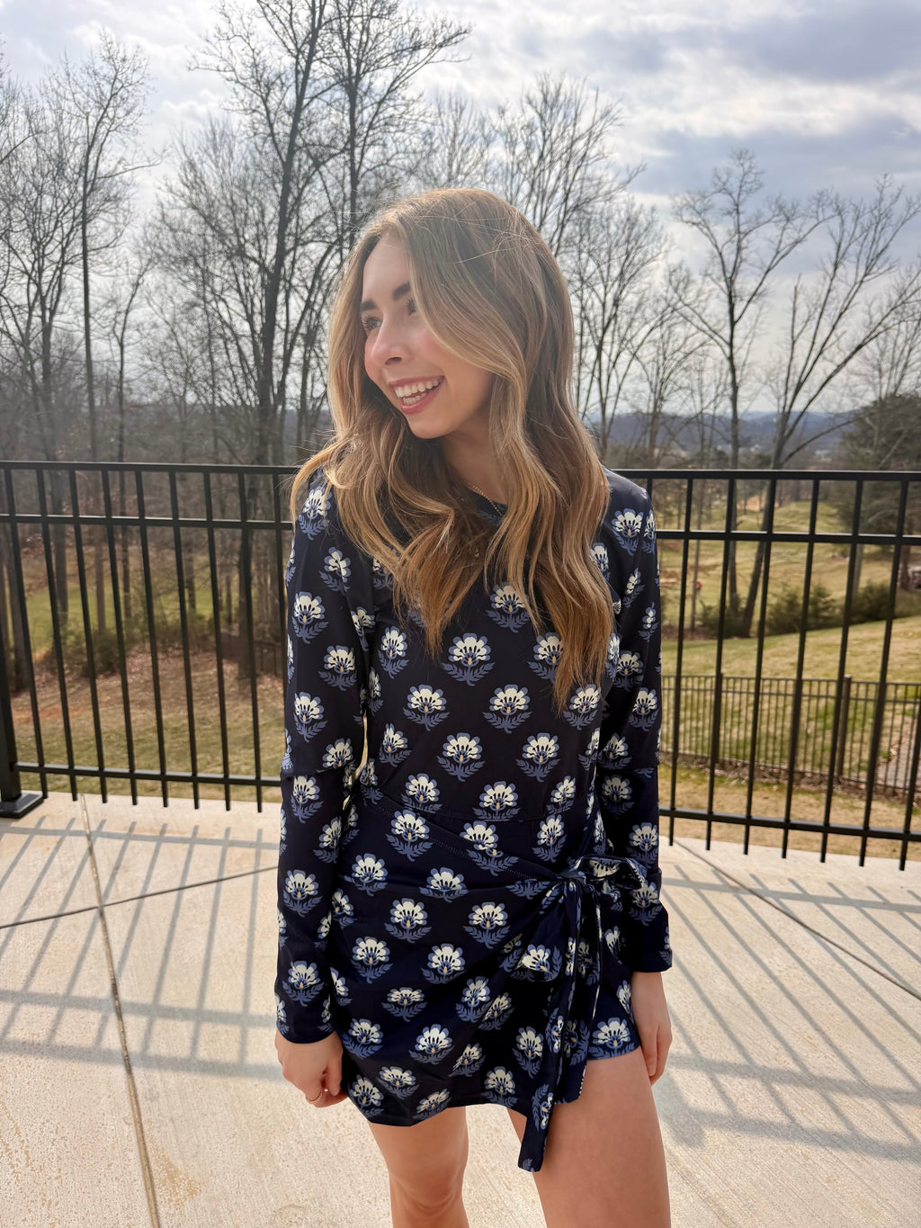 Woman wearing a navy floral dress standing outdoors with trees and sky in the background