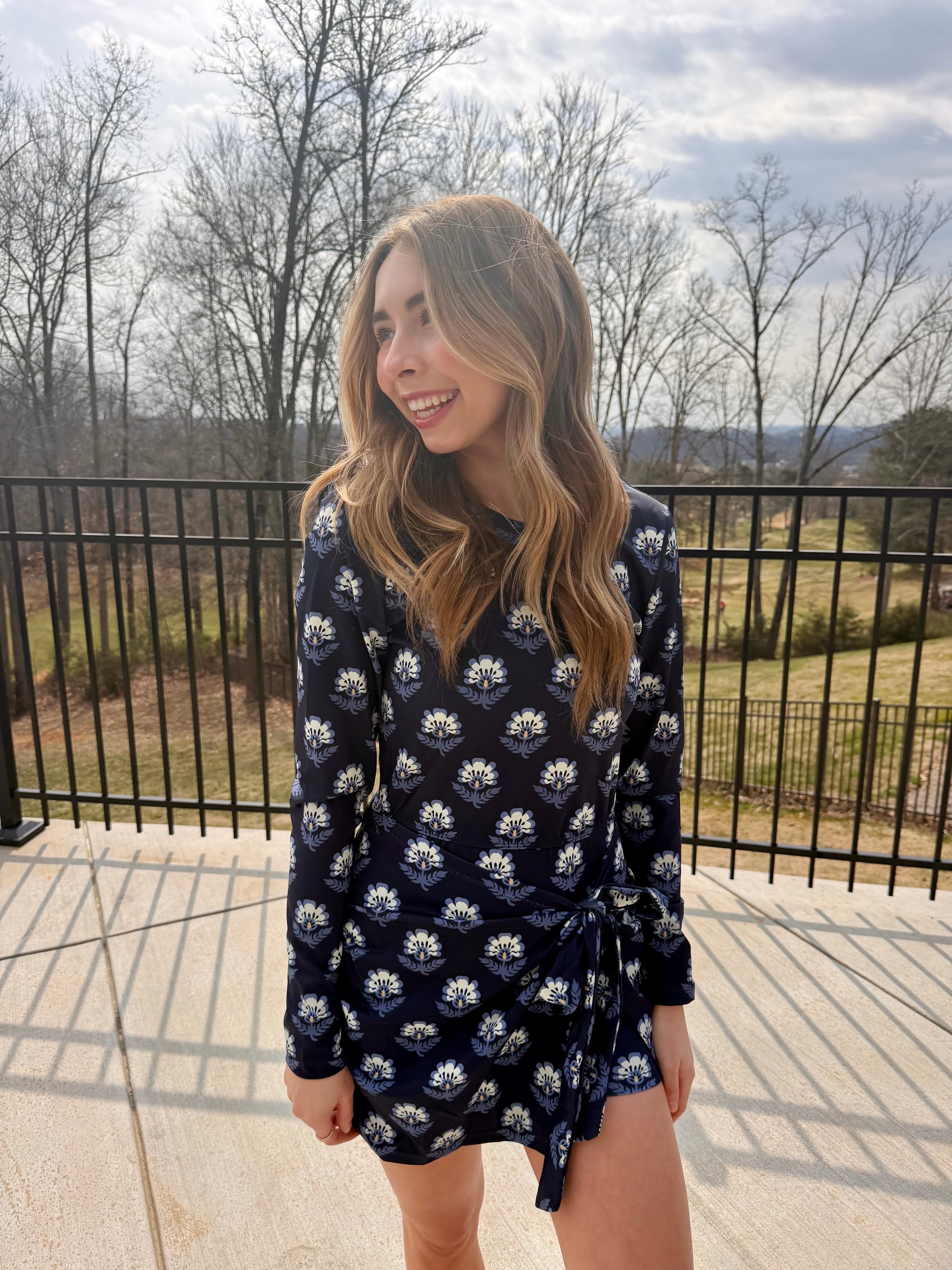Woman wearing a navy floral dress standing outdoors with trees and sky in the background
