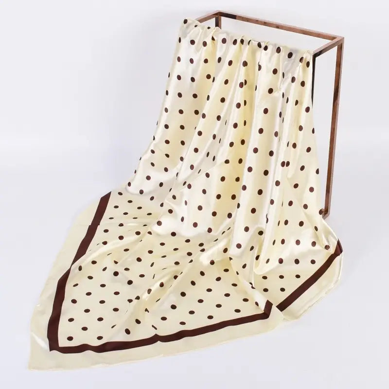 Beige scarf with brown polka dot pattern draped over a wooden frame on a white background