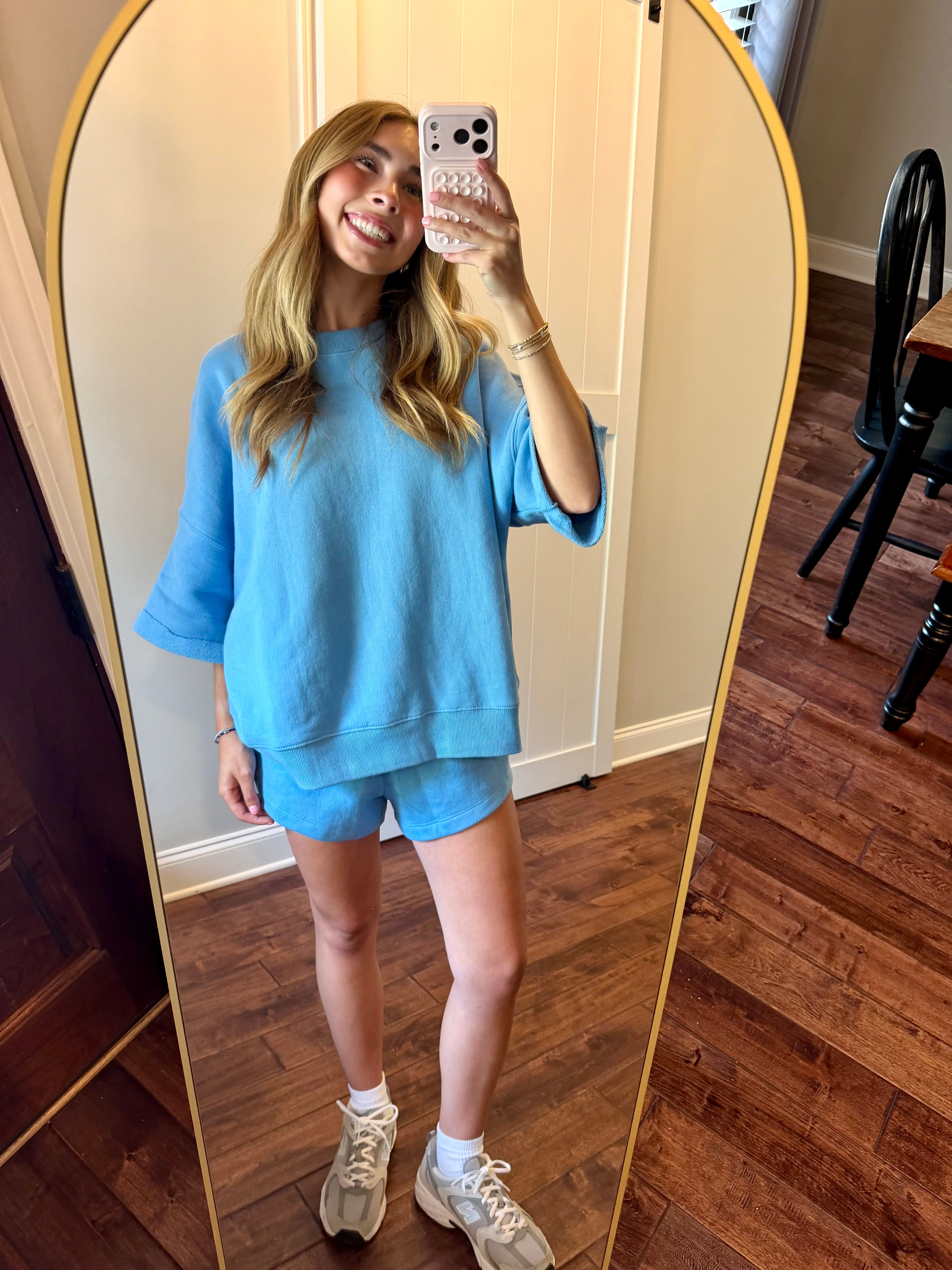 Person wearing a blue outfit taking a mirror selfie in a room with wooden flooring.