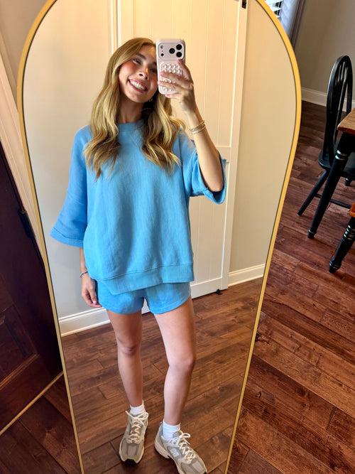 Person wearing a blue outfit taking a mirror selfie in a room with wooden flooring.