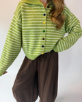 A person wearing a lime green and white striped knit cardigan with colorful buttons, paired with dark brown pants, against a plain light background.