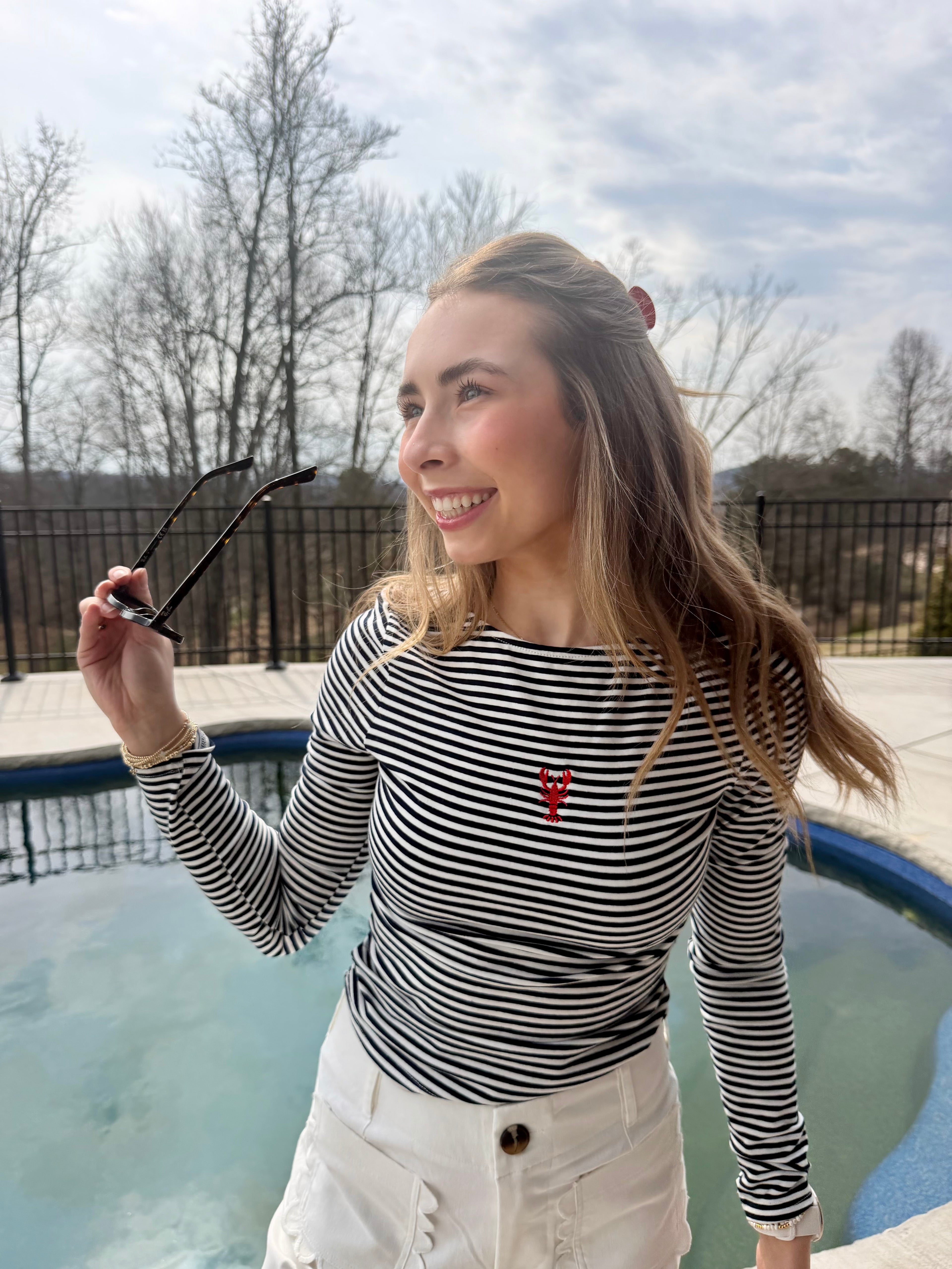 Women in a navy striped tee with a red lobster standing in front of a pool. 