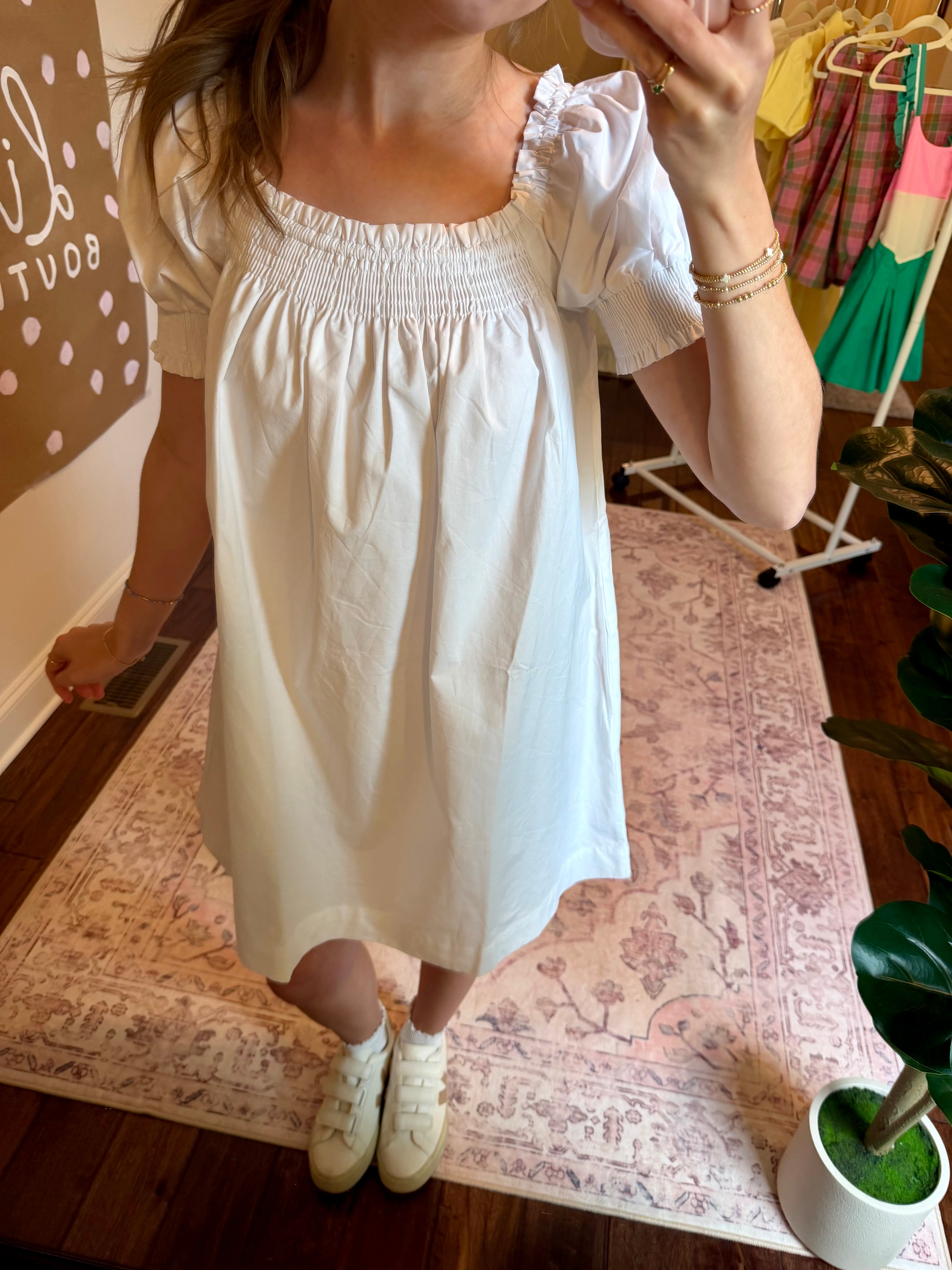 Person wearing a white dress standing on a patterned rug indoors.