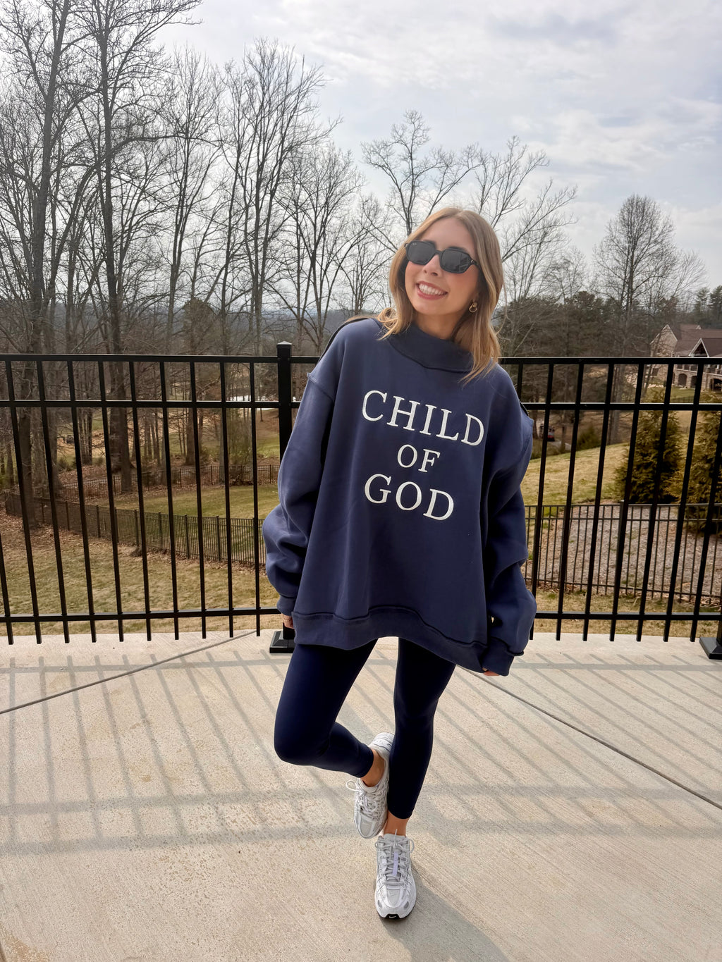 Person wearing a navy sweatshirt with 'CHILD OF GOD' text outdoors.