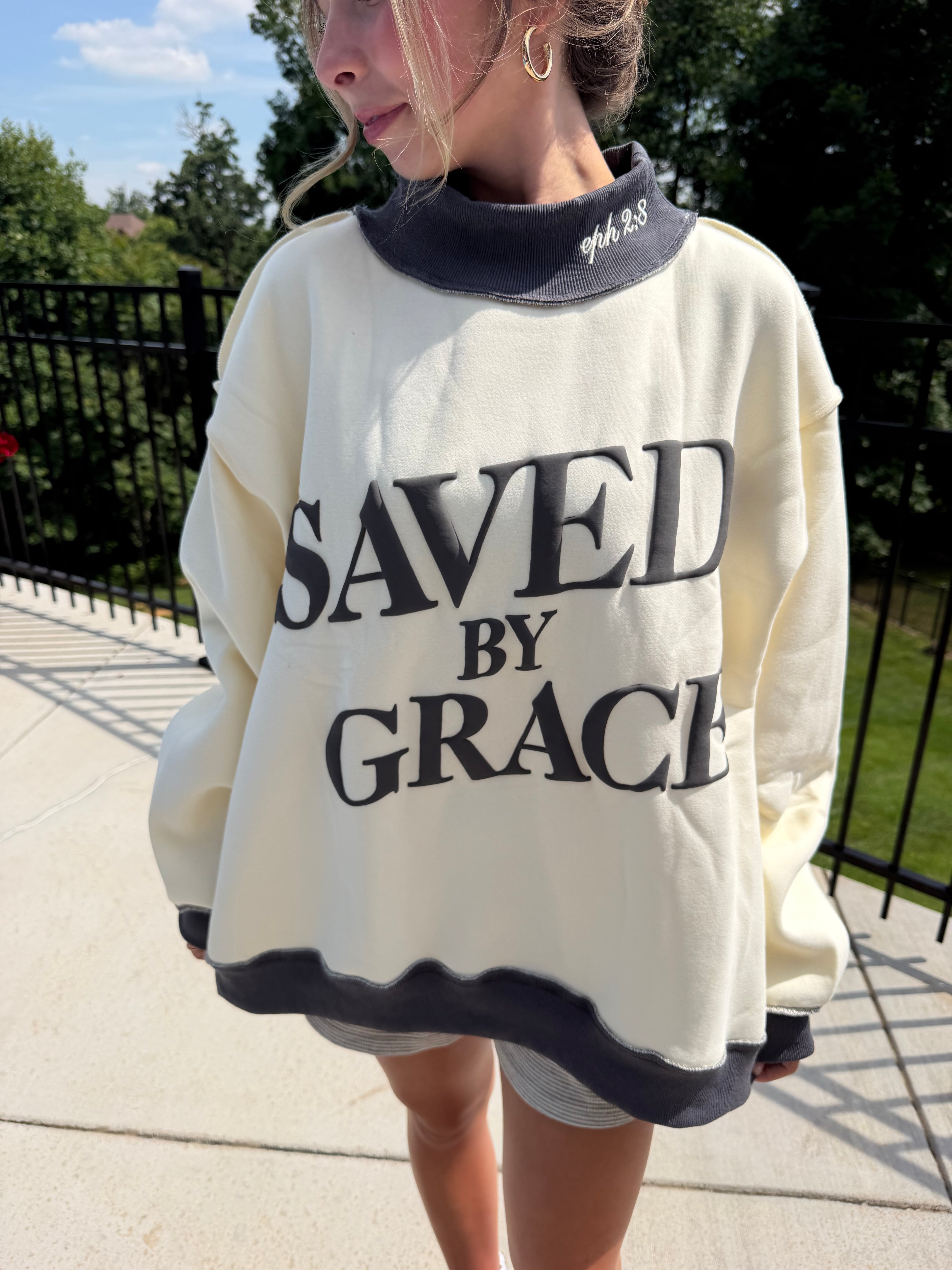 Person wearing a white sweatshirt with 'SAVED BY GRACE' text outdoors.