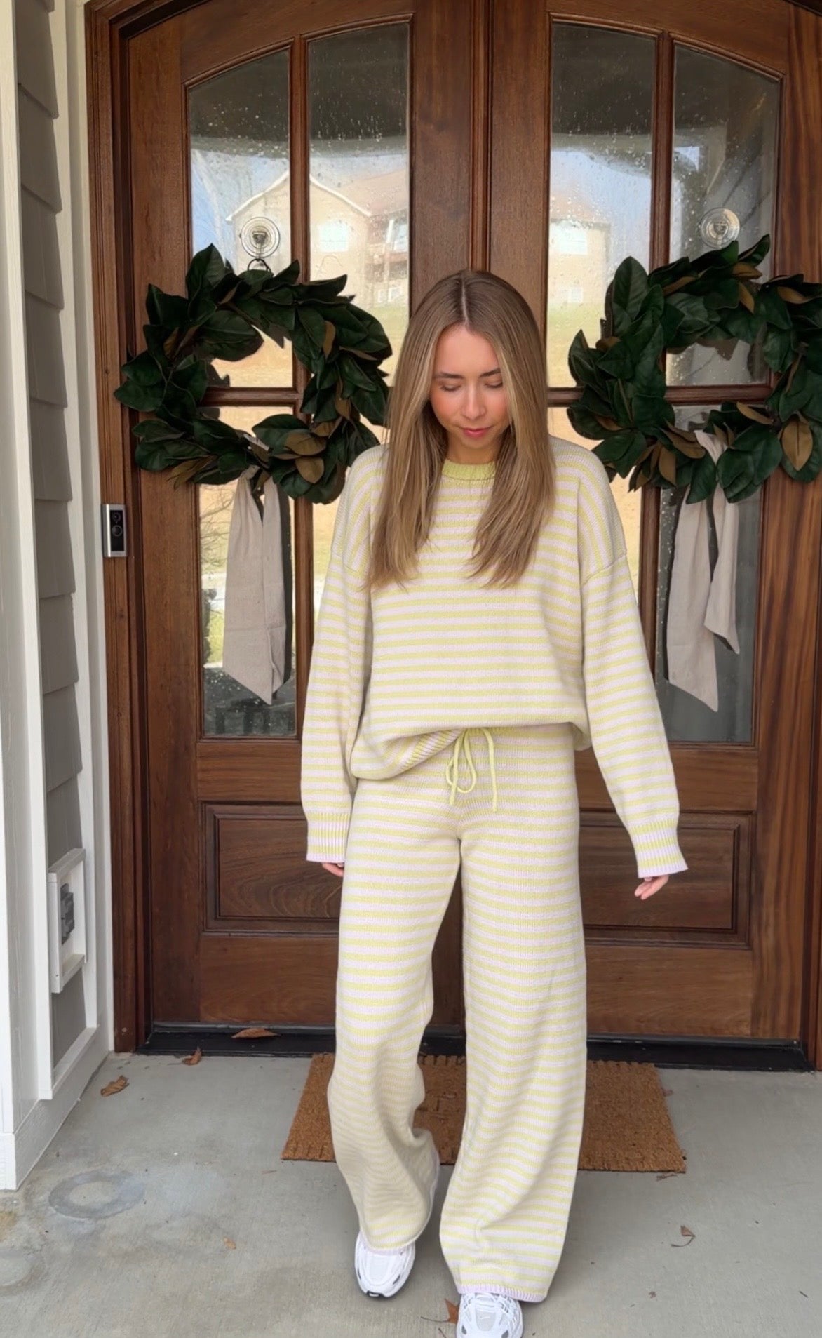 Person wearing a yellow and white striped outfit standing in front of a door with wreaths.
