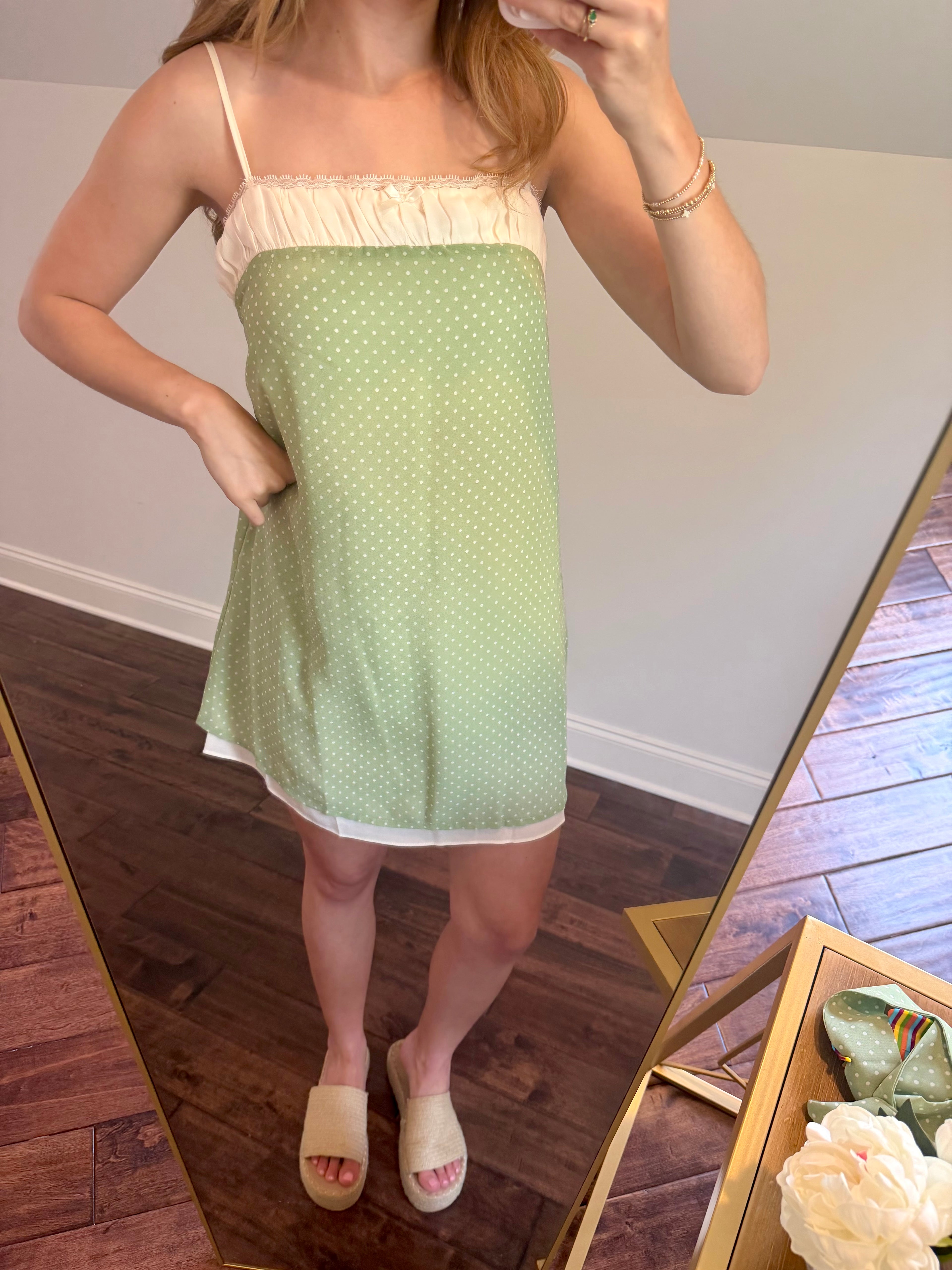 Person wearing a green polka dot dress in front of a mirror.