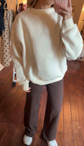 Person wearing a cream sweatshirt and brown pants in a room with wooden flooring.