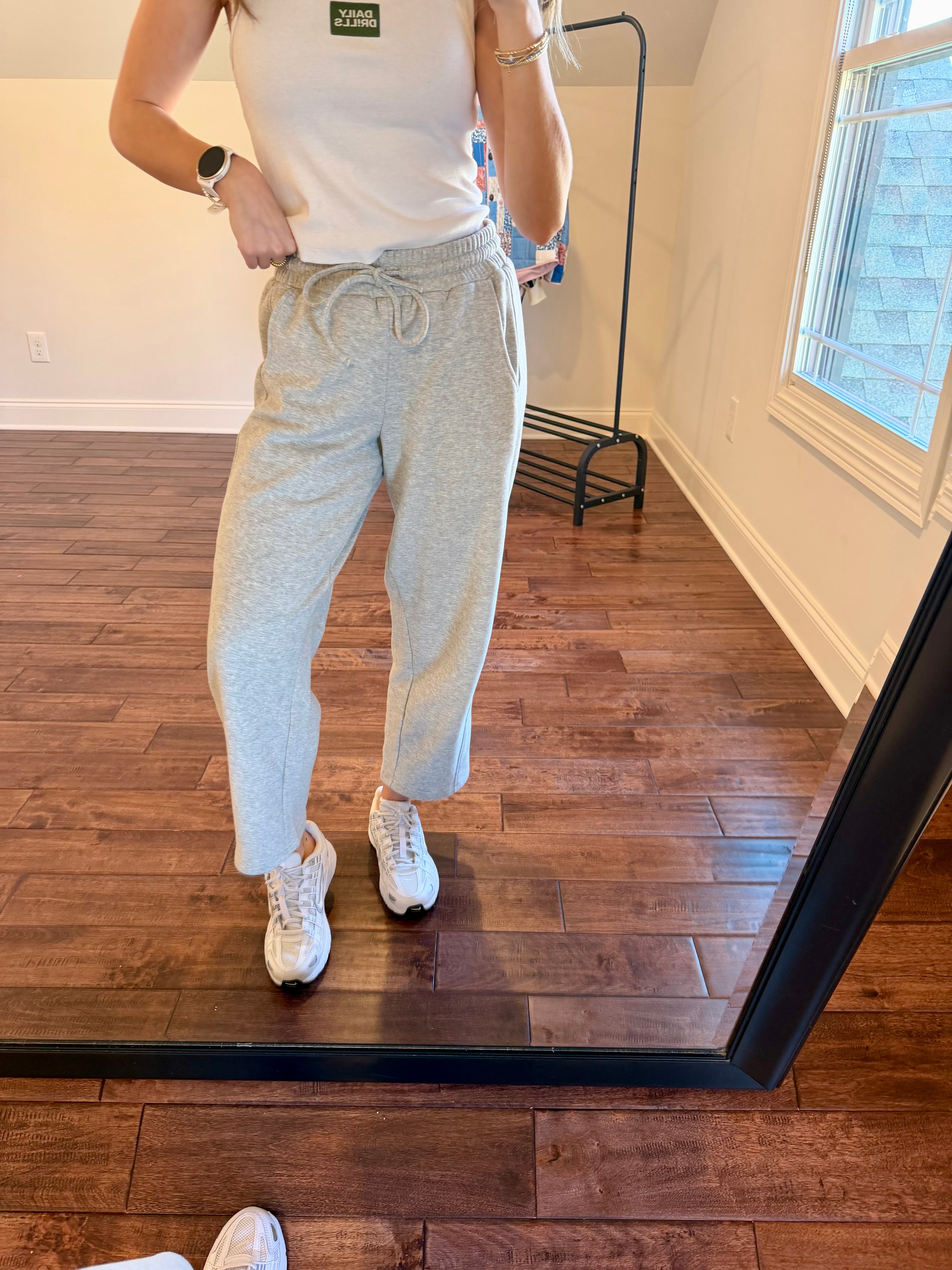 Person wearing a white tank top and gray sweatpants standing in front of a mirror.
