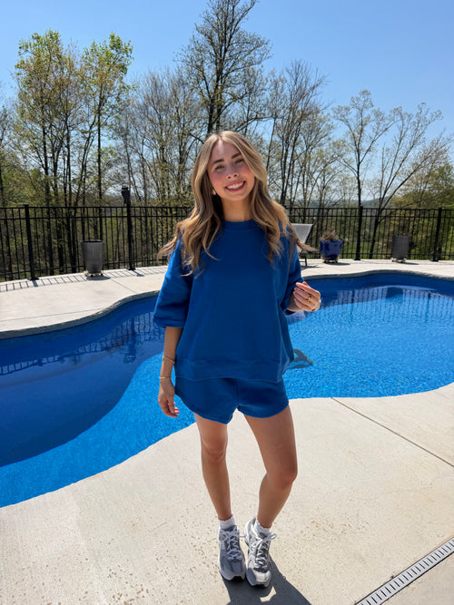 Person in a blue dress standing next to a blue pool with trees and a clear sky in the background.