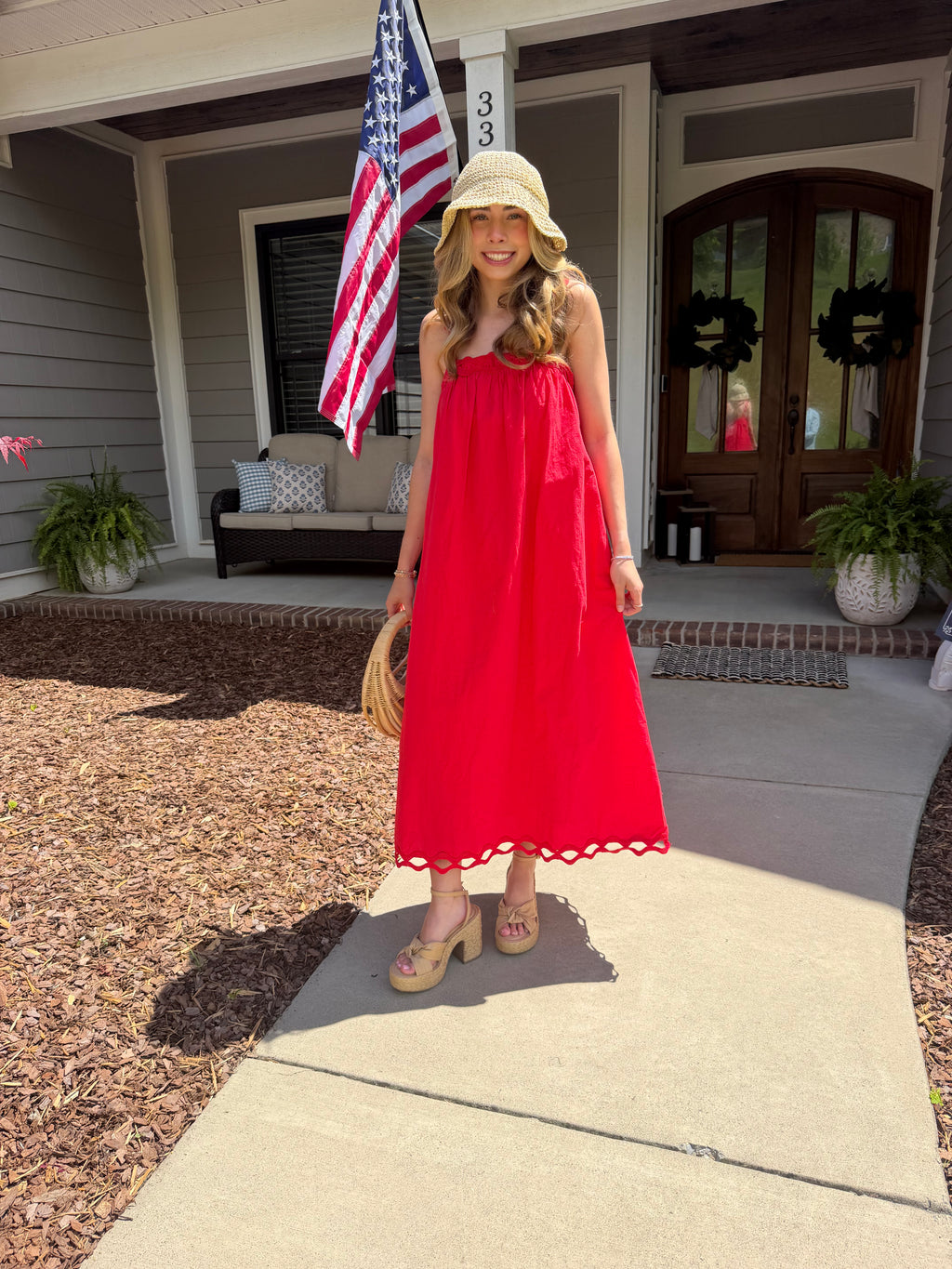 Woman in a red dress standing on a porch with an American flag