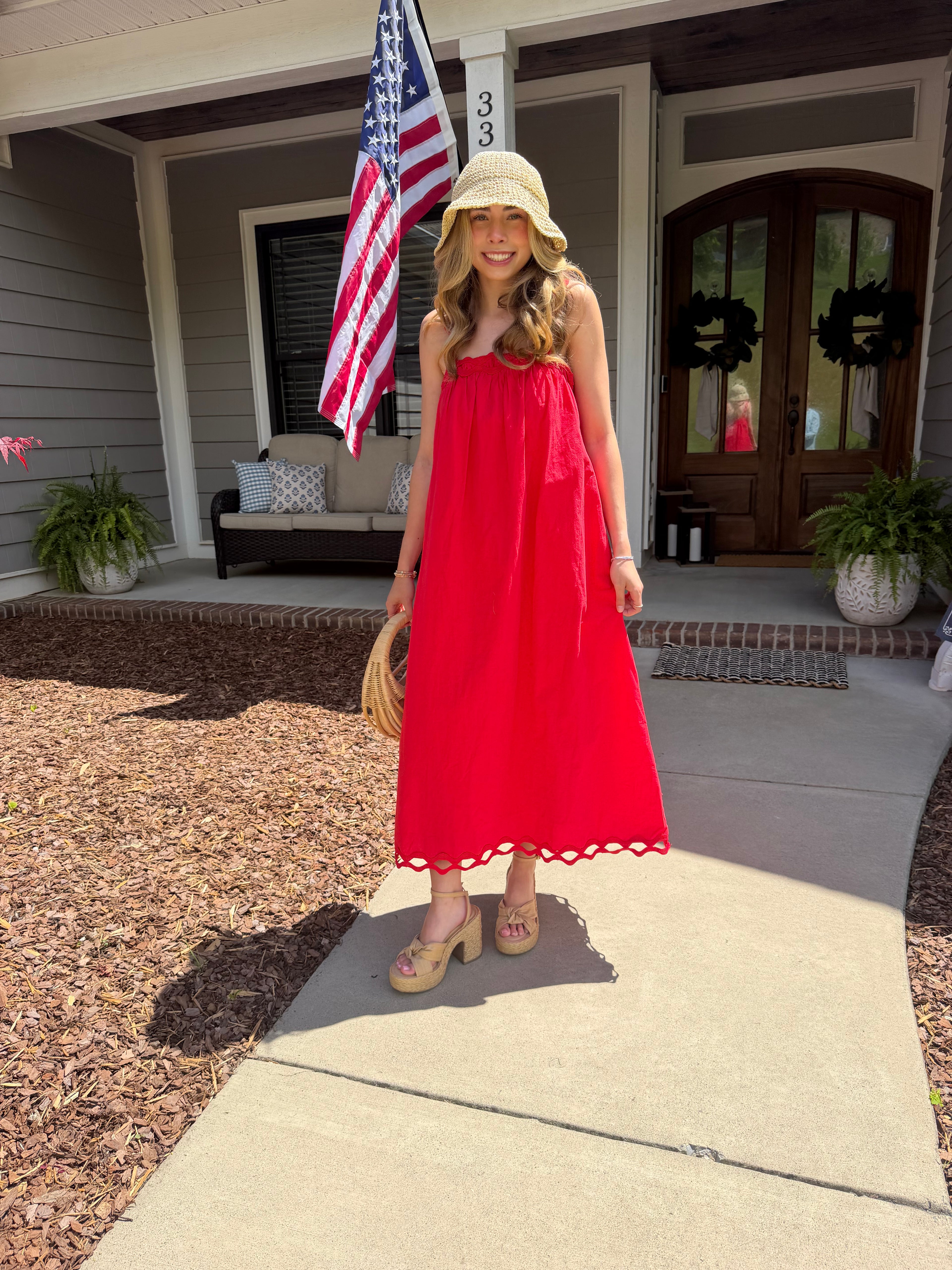 Woman in a red dress standing on a porch with an American flag