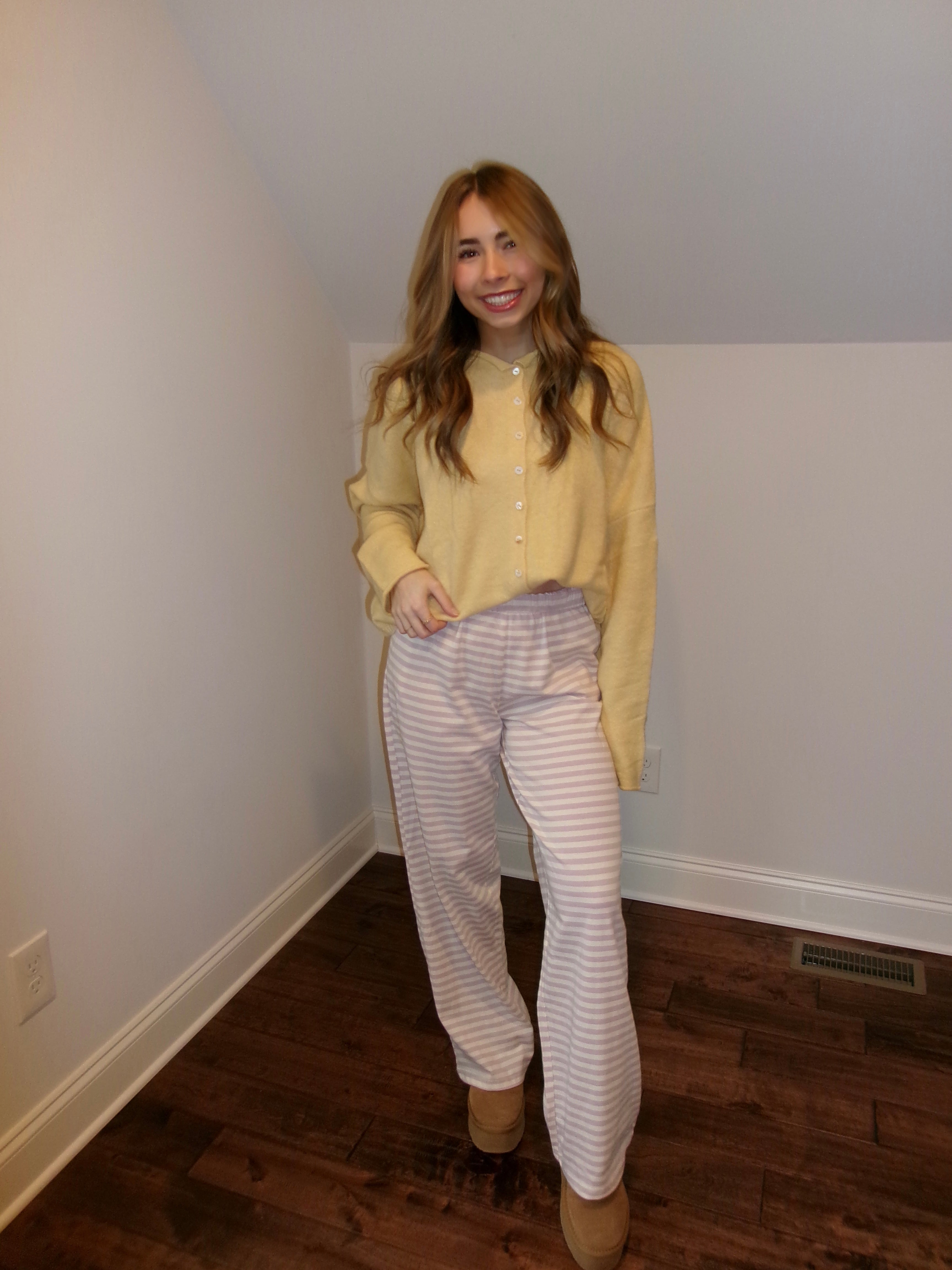 Woman wearing a yellow shirt and striped pants standing in a room with white walls and wooden flooring.