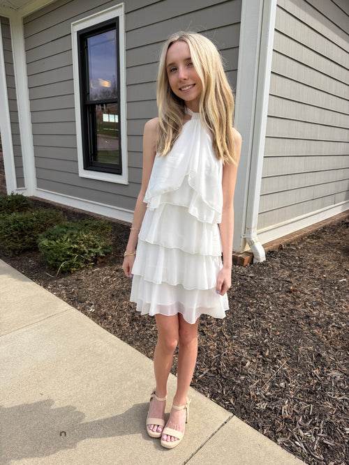 Woman in a white dress standing on a sidewalk next to a house.