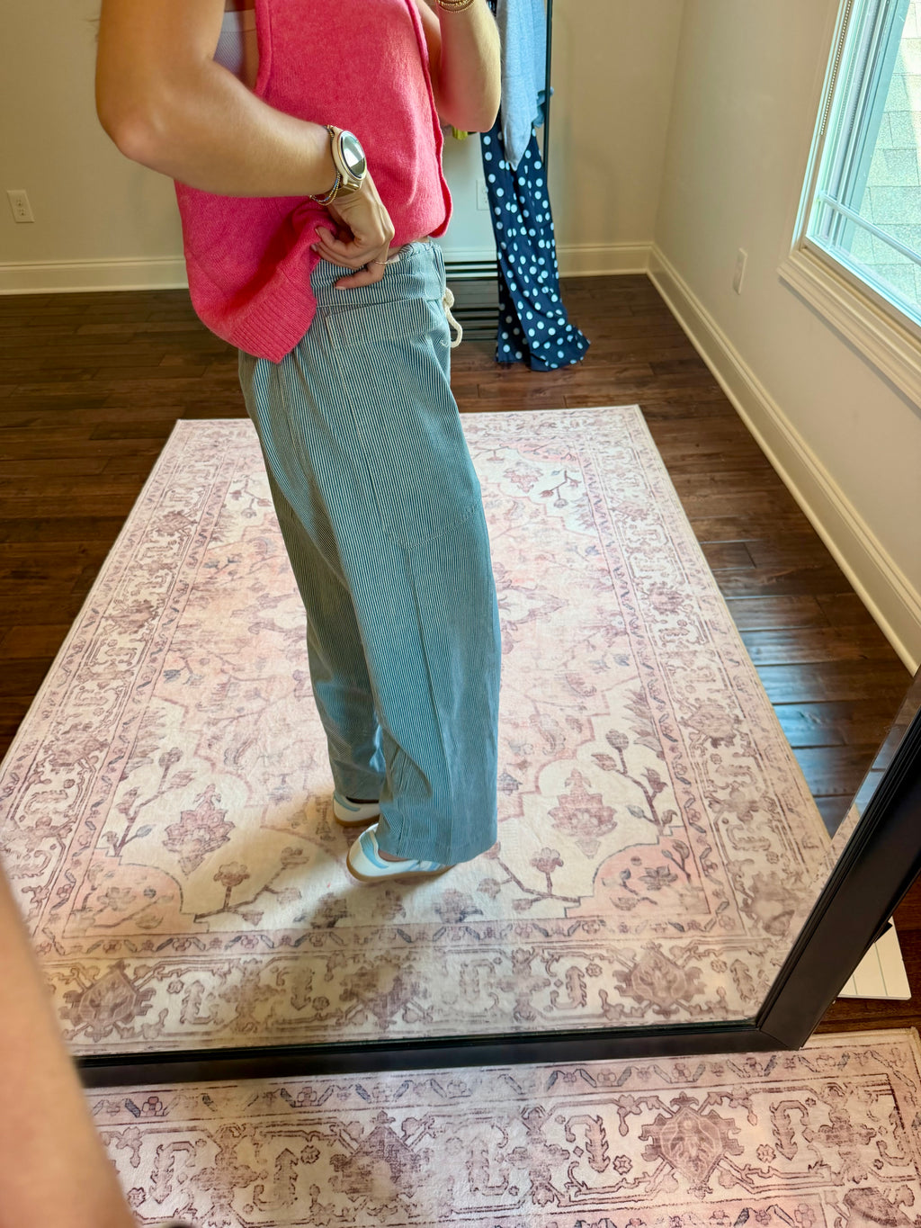 A person standing in a room taking a mirror selfie to show off a pair of wide-leg light blue jeans. The person is also wearing a bright pink sleeveless top and white sneakers.