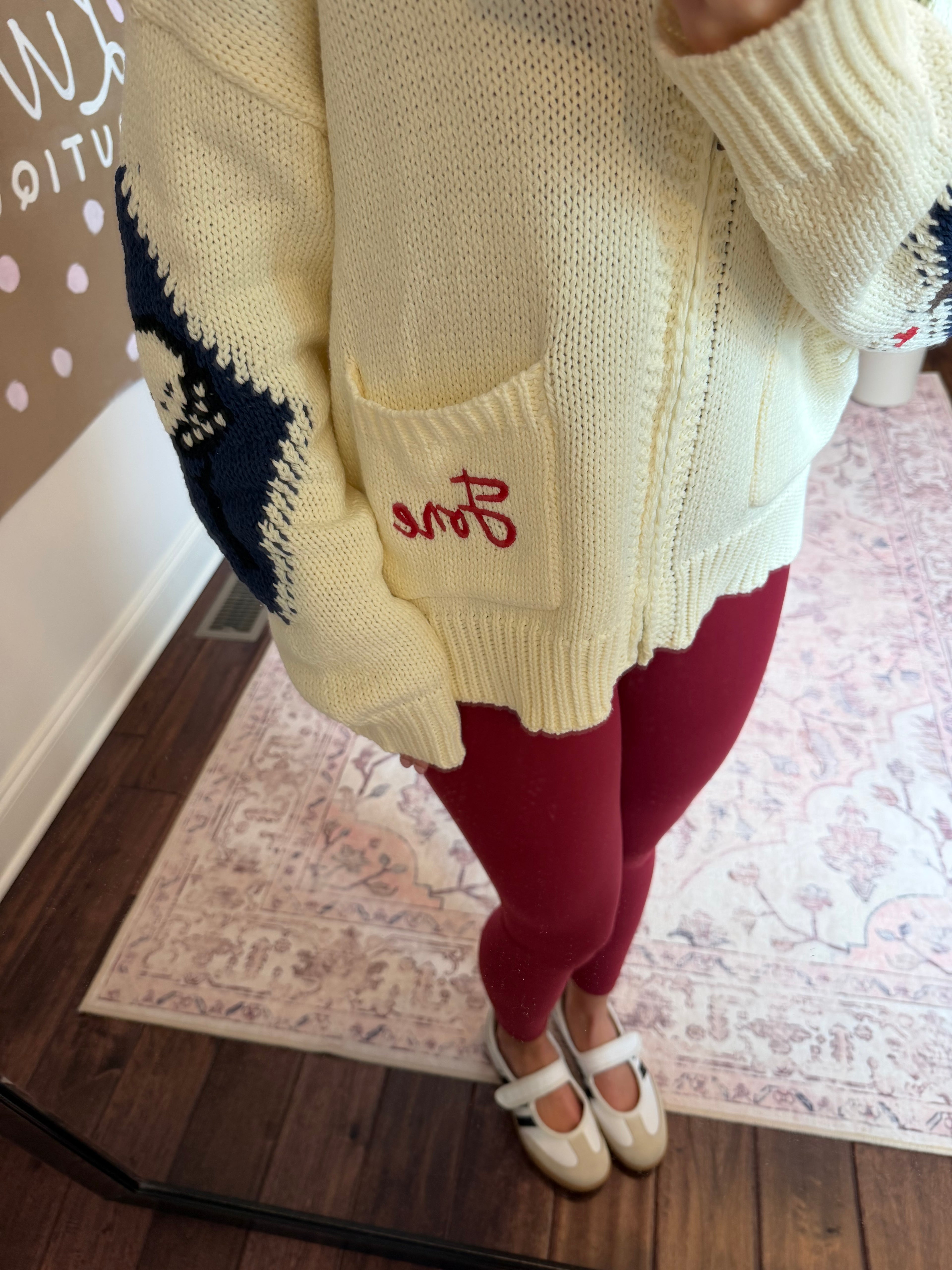 Person wearing a white sweater with green and red patterns, standing on a patterned rug.