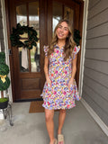 Woman in a floral dress standing in front of a wooden door with a wreath.