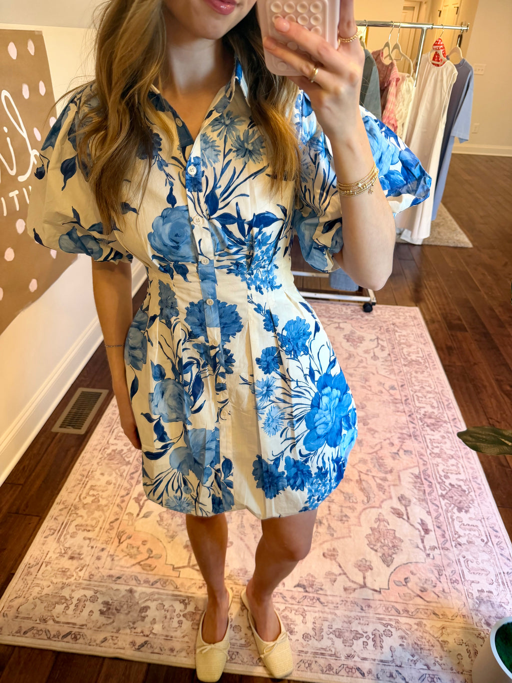 Woman taking a mirror selfie wearing a blue floral dress in a room with plants and a chandelier.