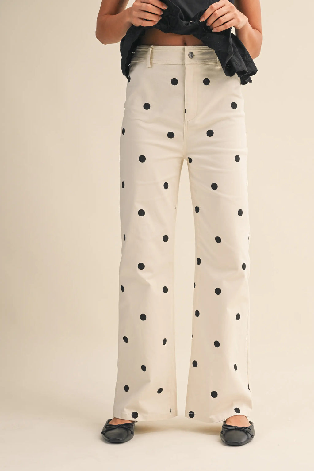 White pants with black polka dots worn by a person on a beige background