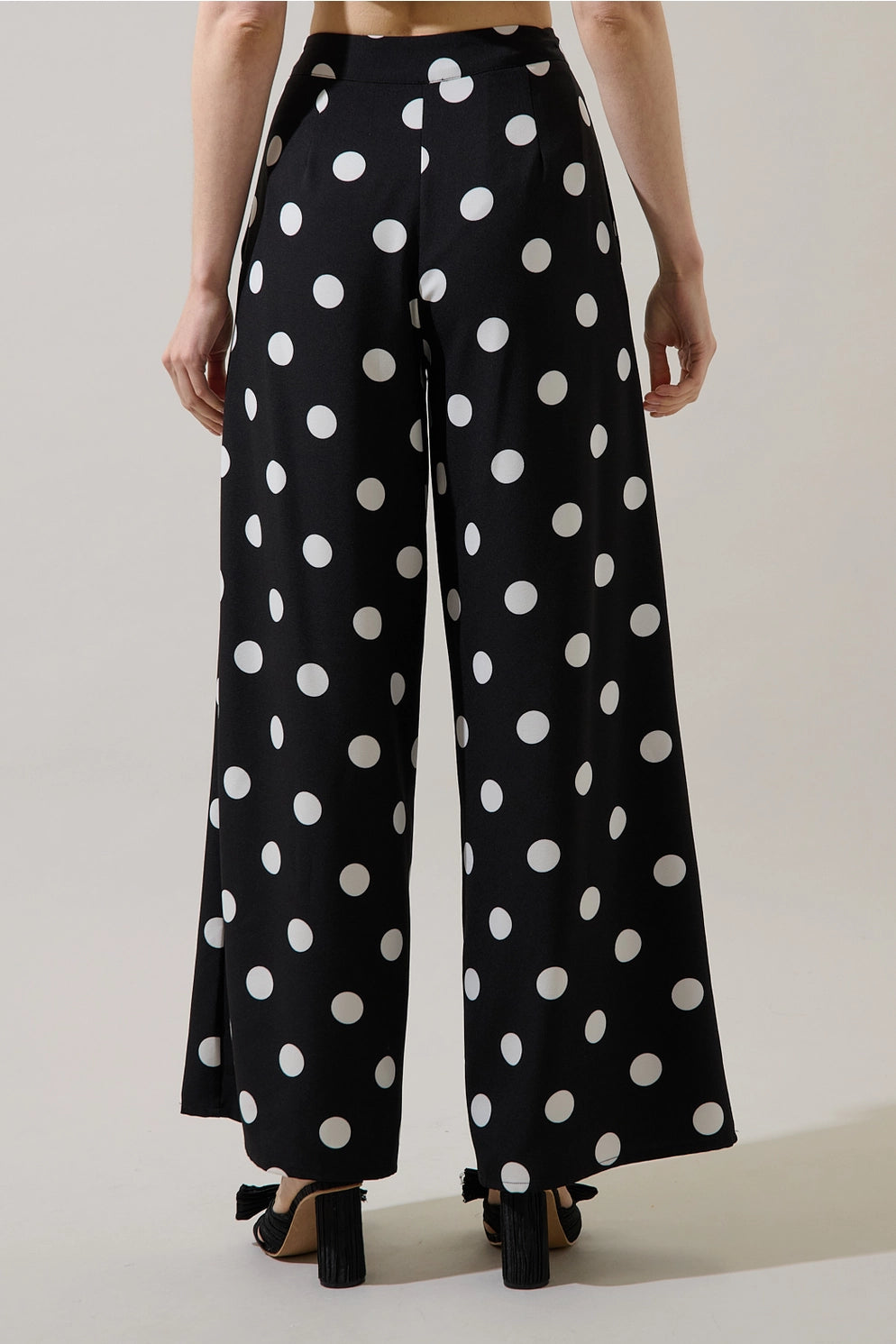 Black wide-leg trousers with a white polka dot pattern, shown on a model from the back against a light beige studio background.