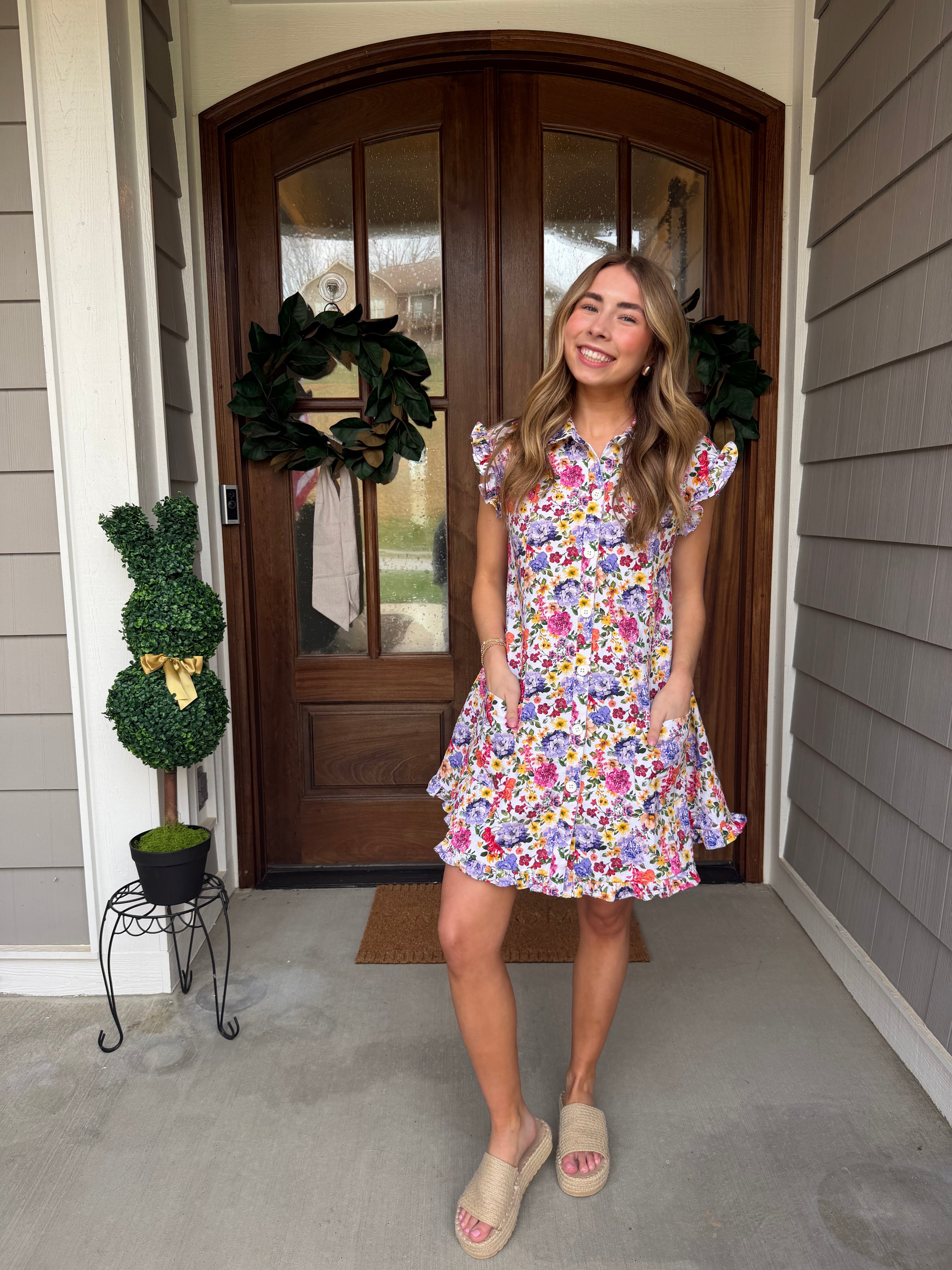 Woman in a floral dress standing in front of a wooden door with wreaths.