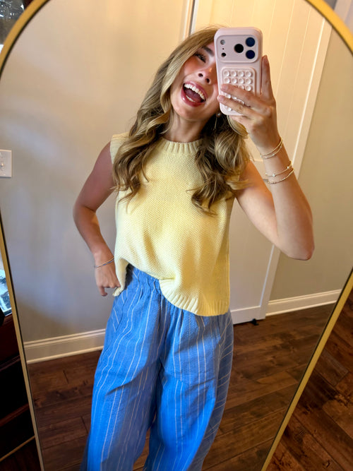 Person taking a mirror selfie wearing a yellow top and blue pants.