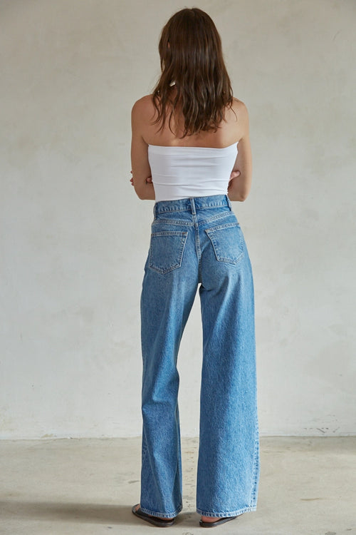 Woman wearing a white strapless top and blue jeans against a plain background