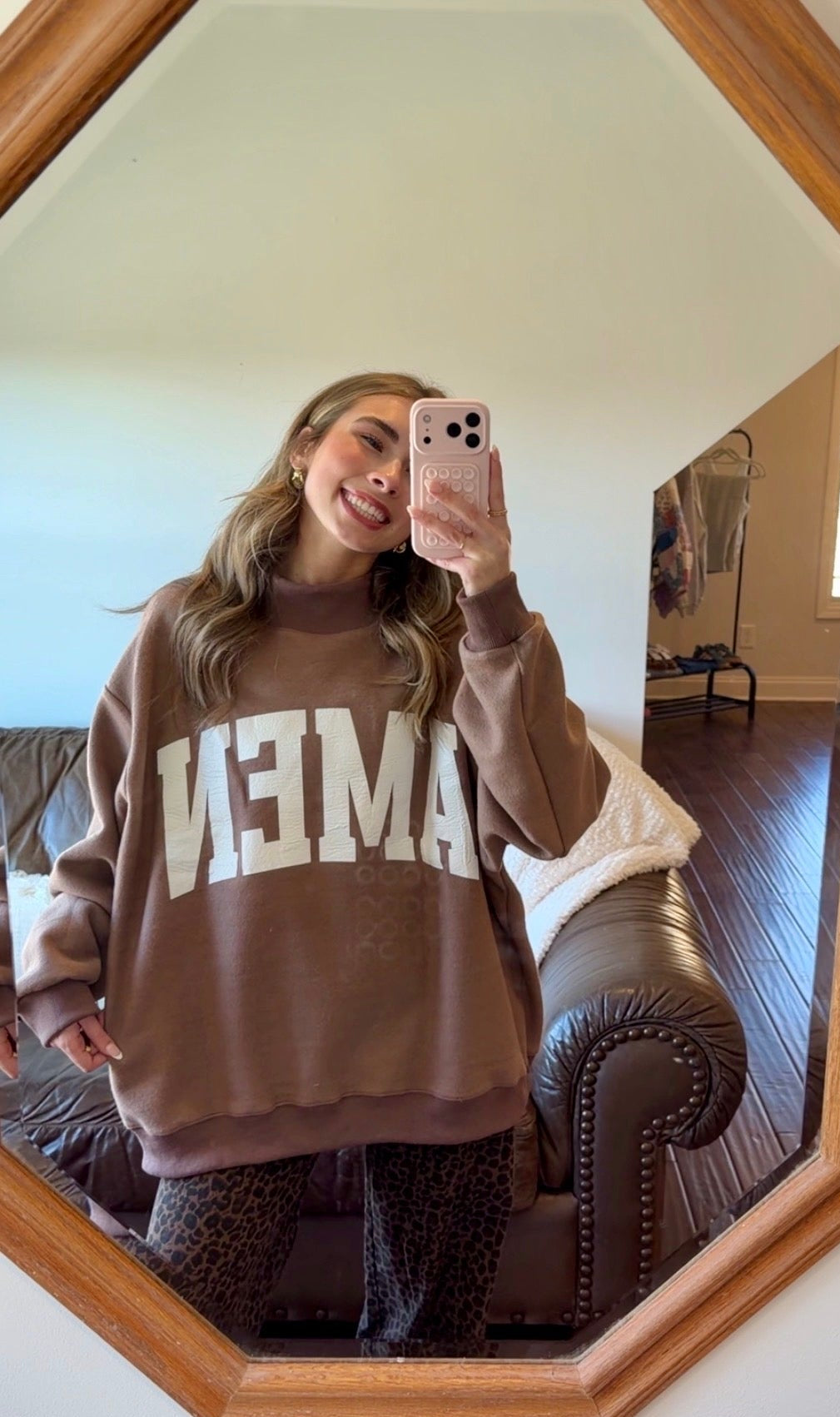 Person wearing a brown sweatshirt with 'WWJD’ text, taking a mirror selfie.
