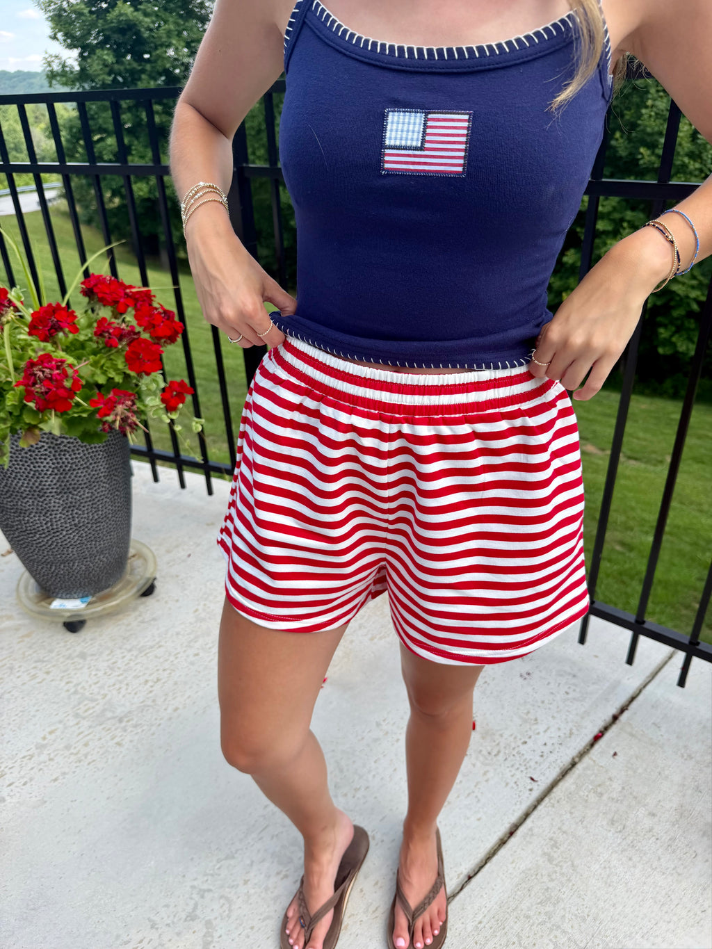 Person wearing a navy tank top with an American flag design and red and white striped shorts on a patio.