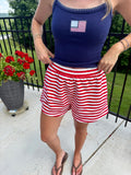 Person wearing a navy tank top with an American flag design and red and white striped shorts on a patio.