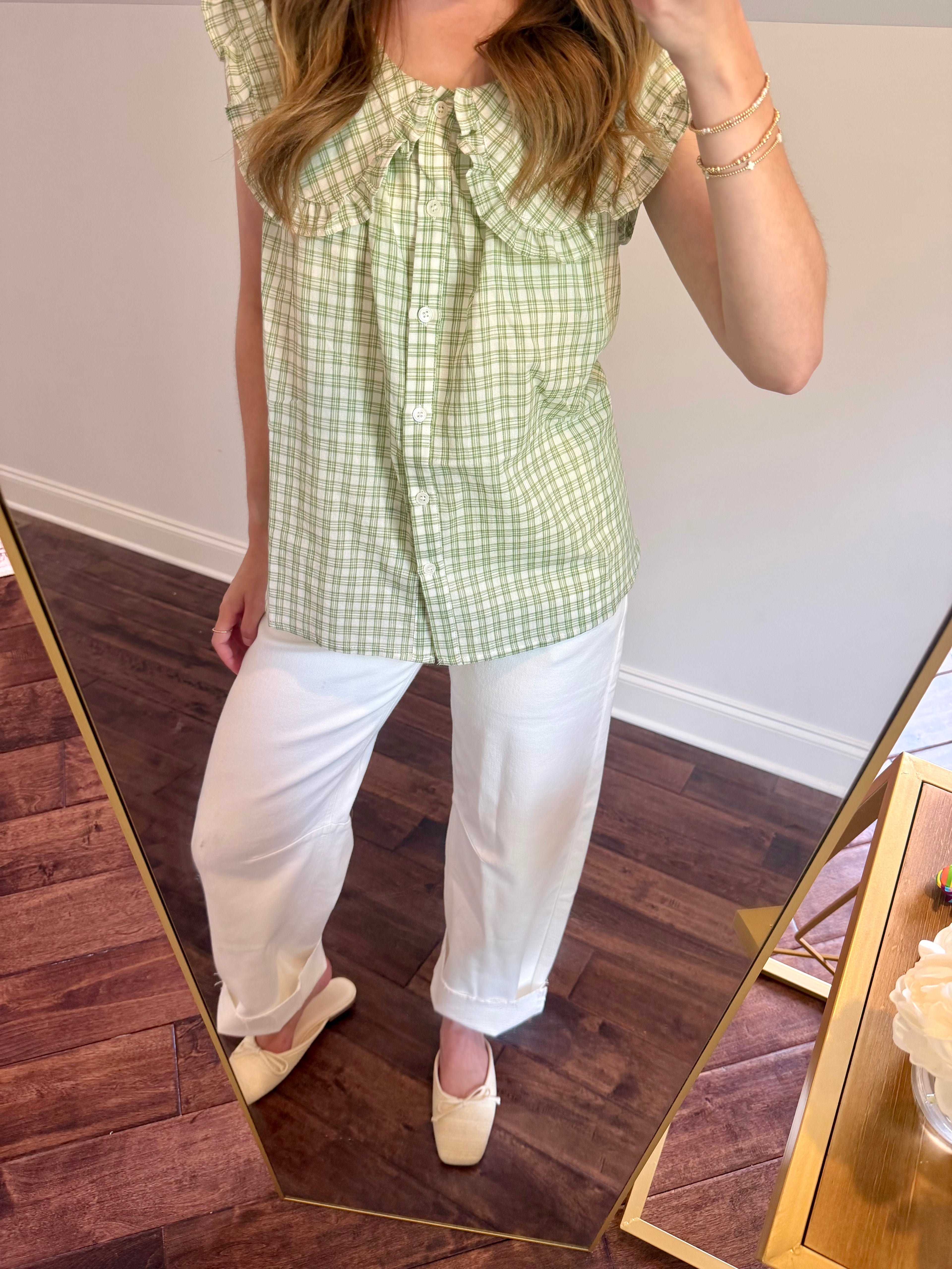 Person wearing a green checkered top and white pants standing in front of a mirror.