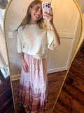 Woman taking a mirror selfie wearing a white top and pink floral skirt.