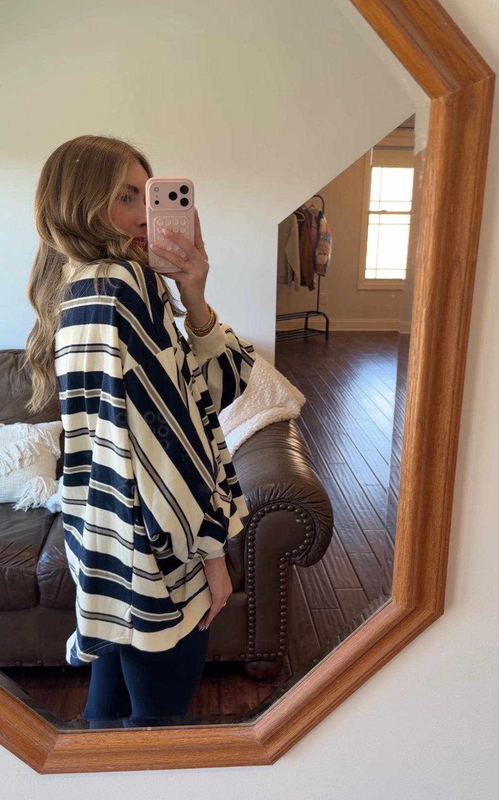 Person wearing a striped poncho taking a mirror selfie in a living room.