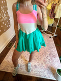 Person wearing a colorful dress with a pink top and green skirt in a room.