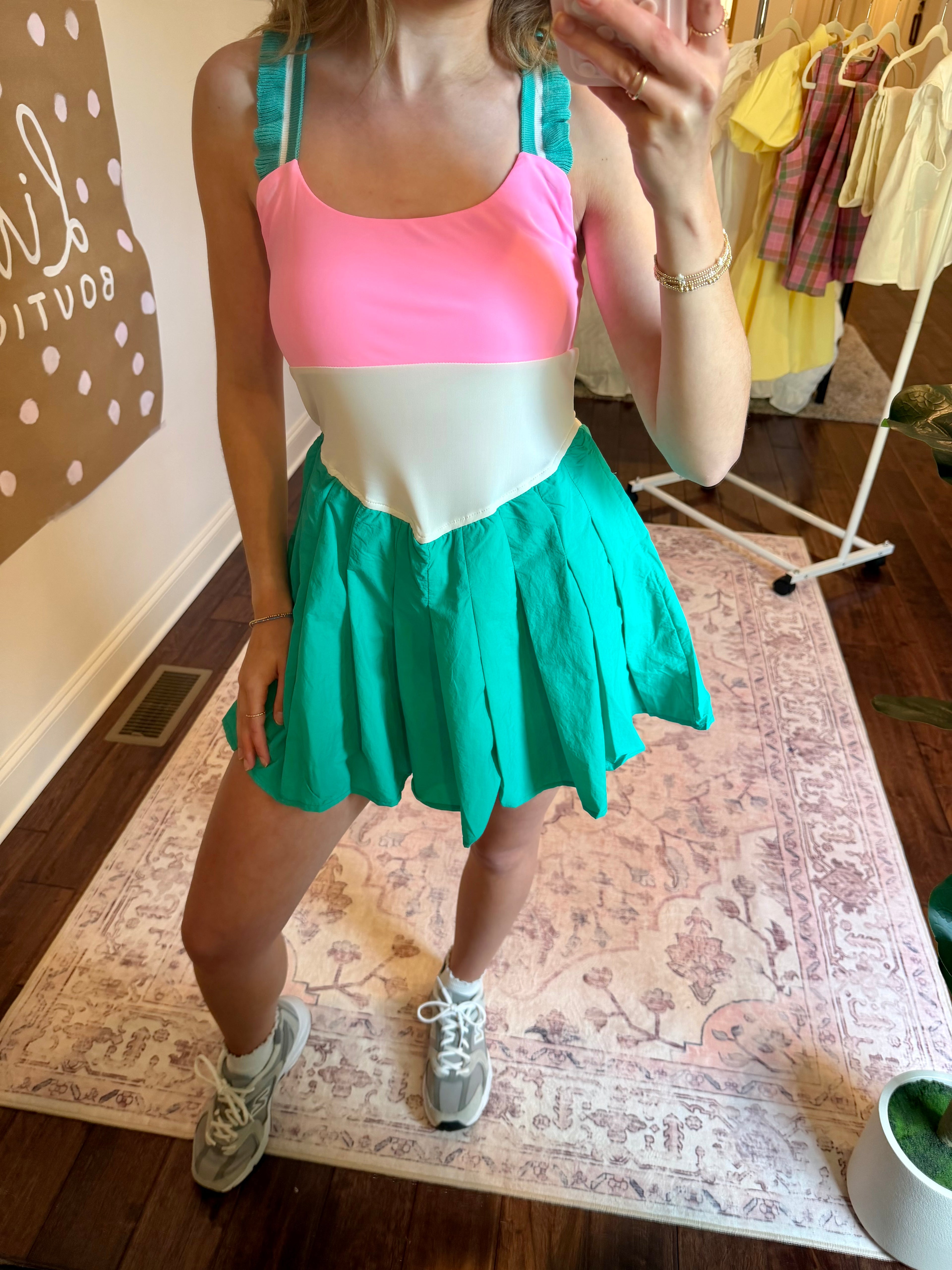 Person wearing a colorful dress with a pink top and green skirt in a room.