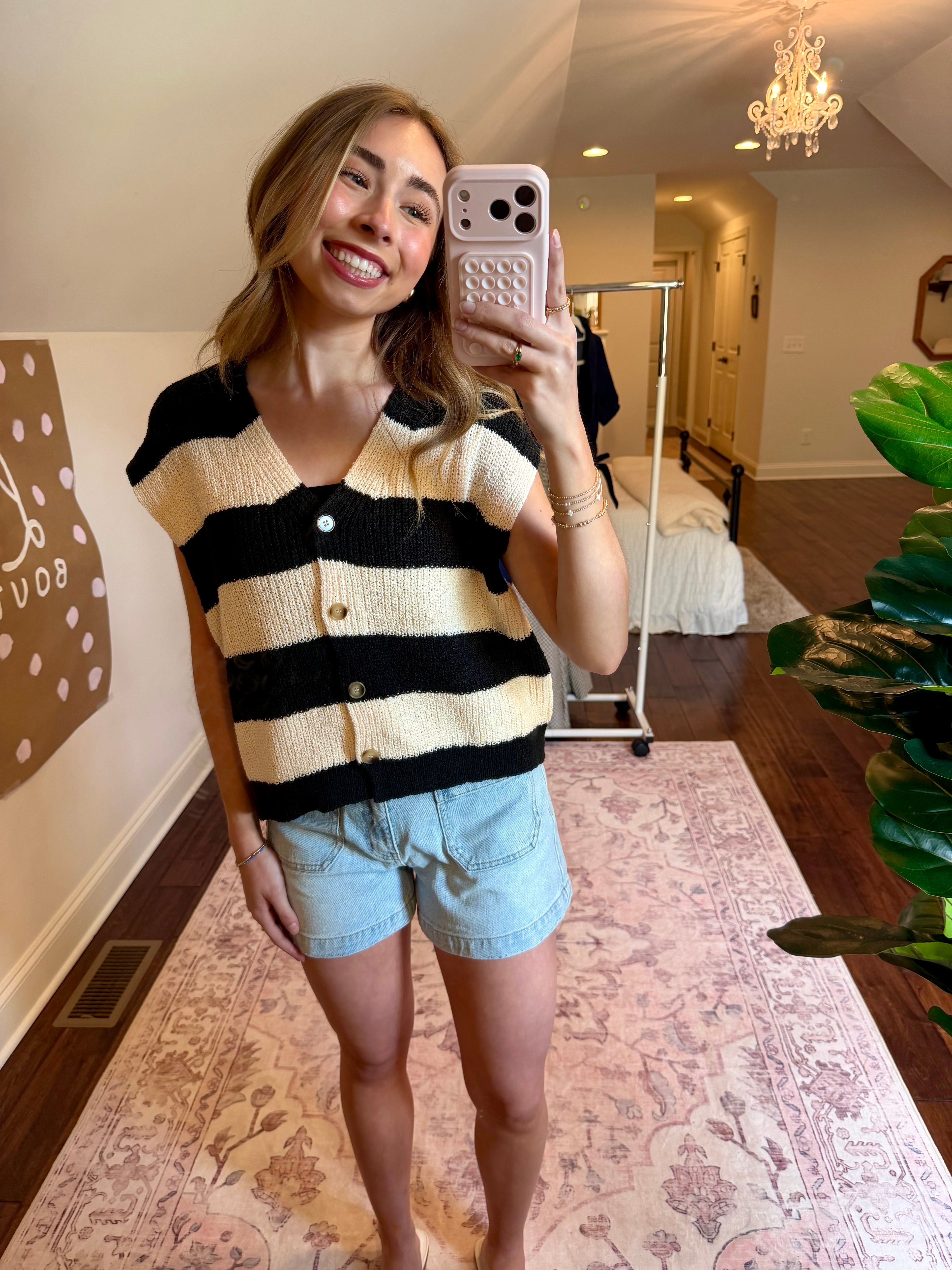Woman taking a mirror selfie wearing a striped sweater and denim shorts in a home setting.