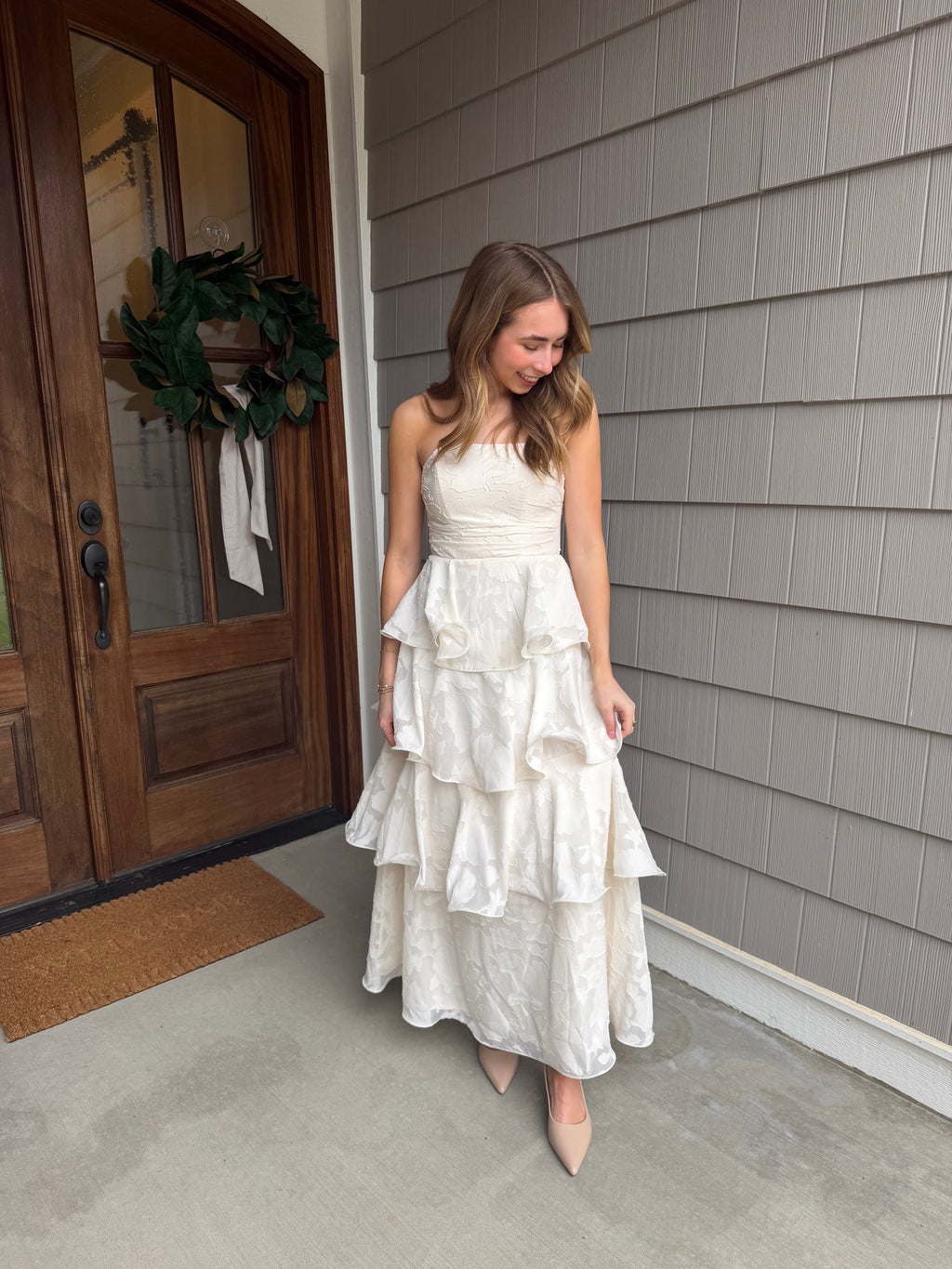 Woman in a white dress standing in front of a wooden door with a gray wall background
