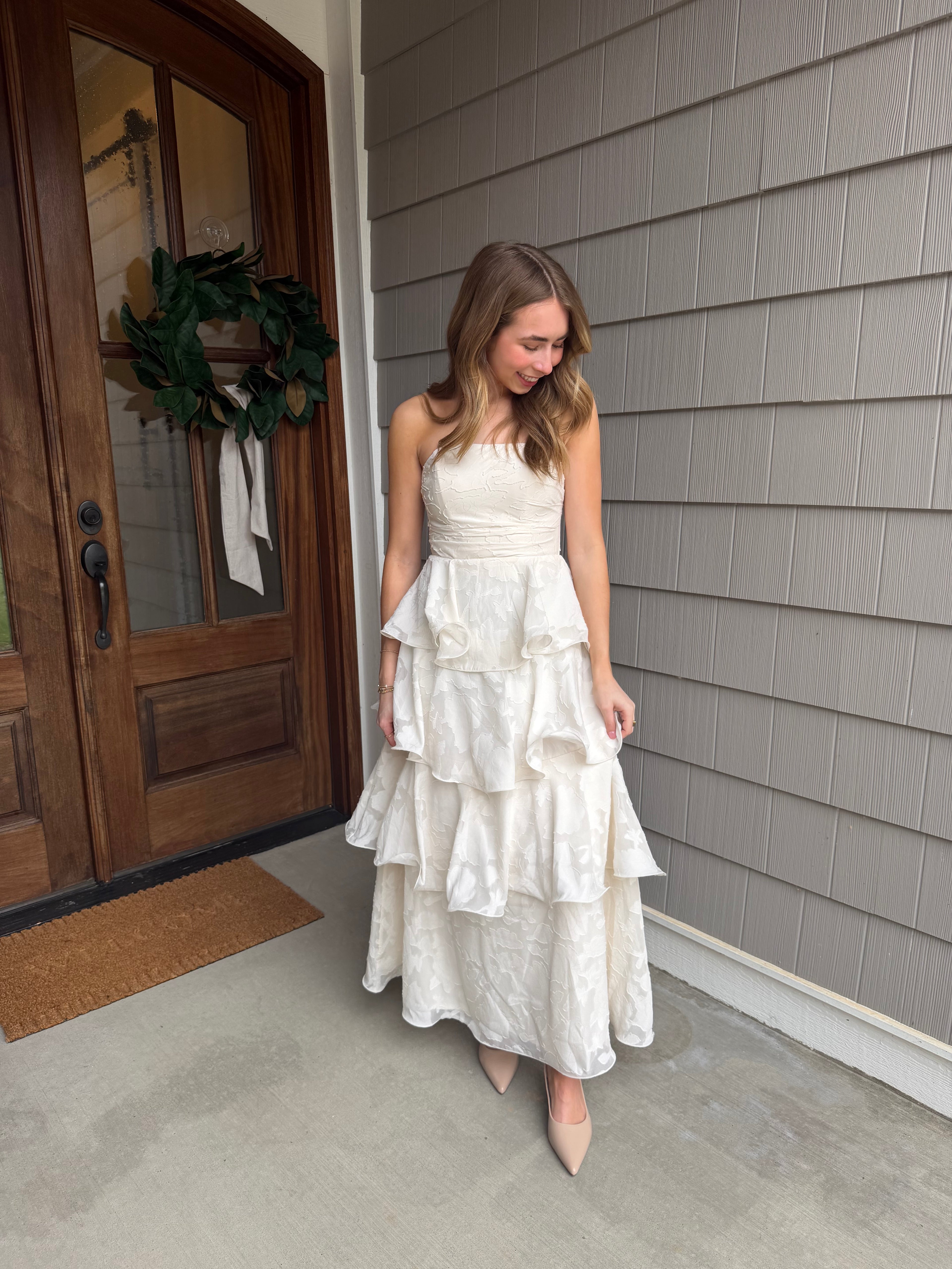 Woman in a white dress standing in front of a wooden door with a gray wall background