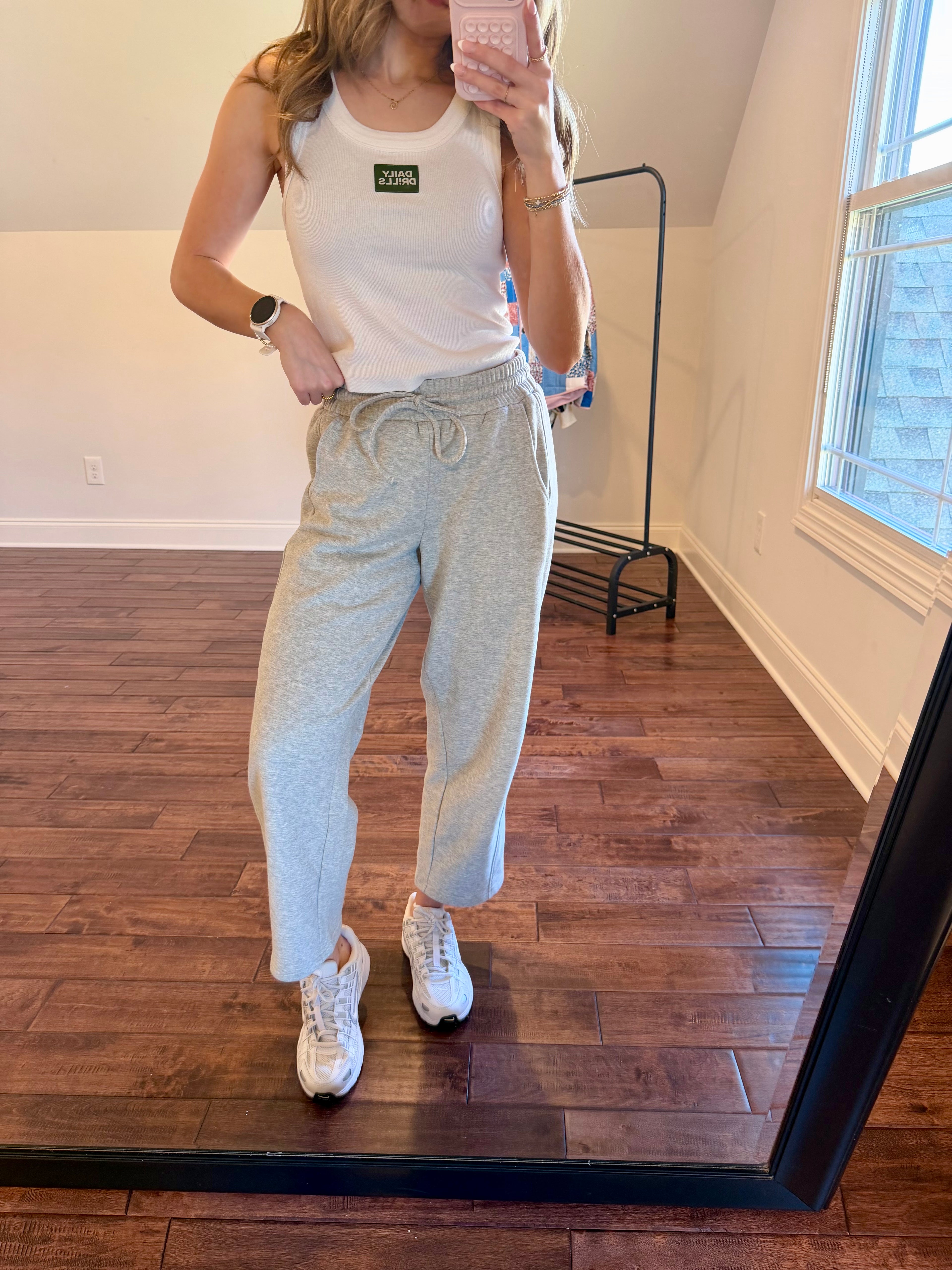 Person wearing a white tank top and gray sweatpants standing in front of a mirror.