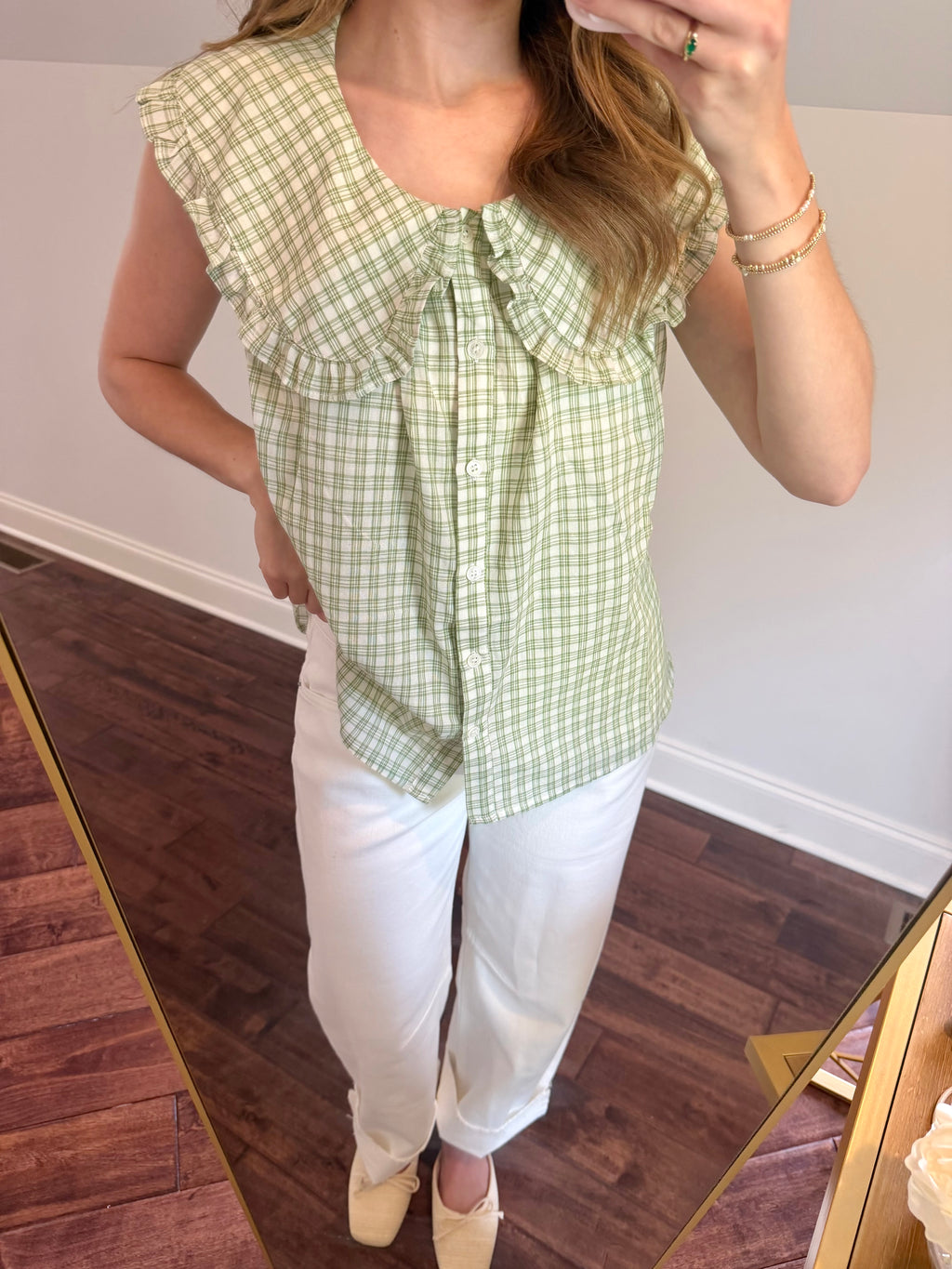 Person wearing a green checkered top and white pants in front of a mirror.