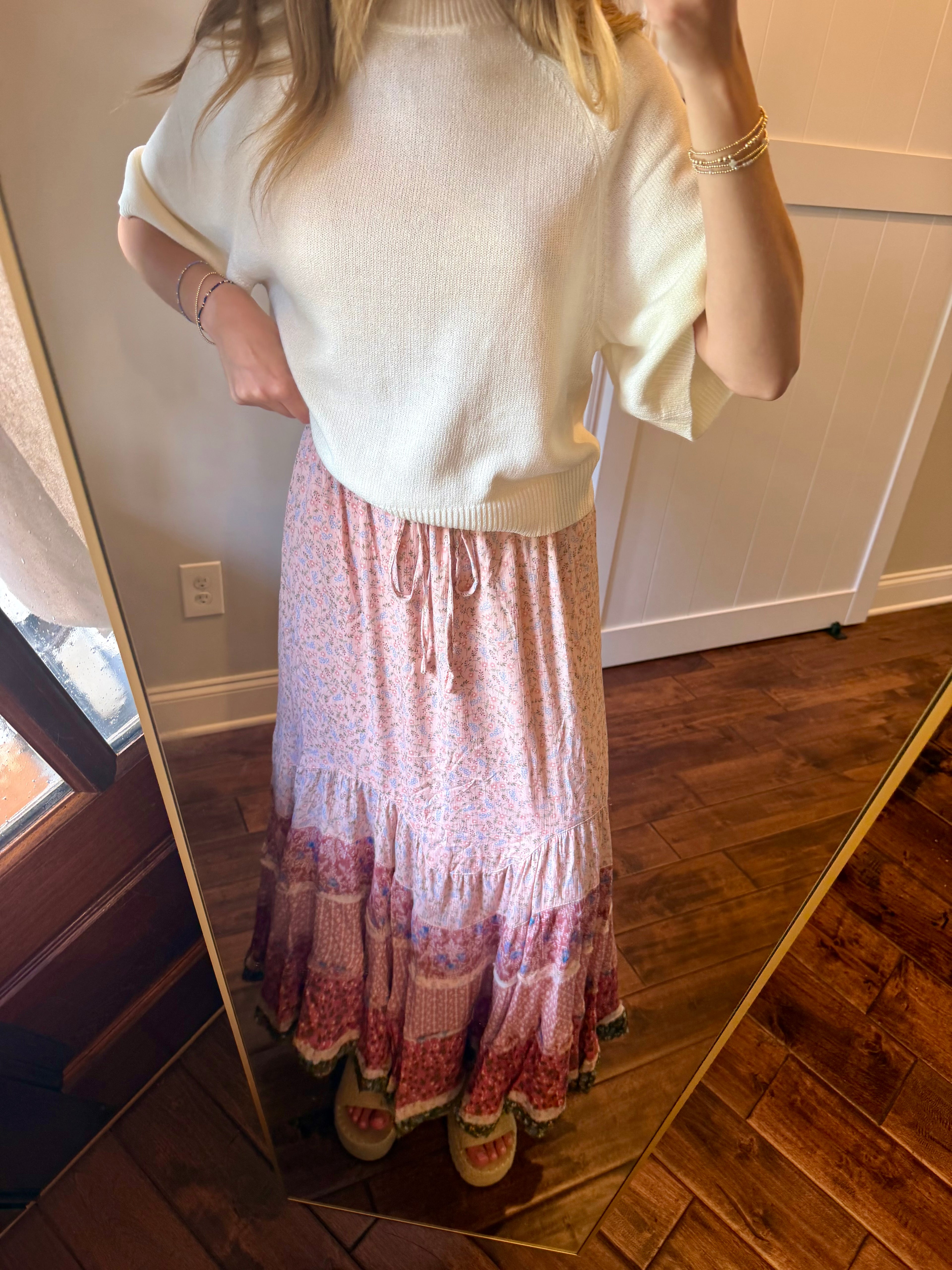 Person wearing a white sweater and pink patterned skirt standing in front of a mirror.