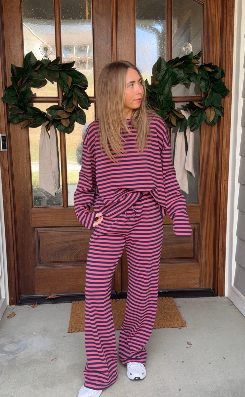 Person wearing a purple and pink striped outfit standing in front of a wooden door with wreaths.
