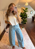 Woman taking a mirror selfie wearing a white top and light blue pants with a polka dot pattern in a room with a plant and rug.