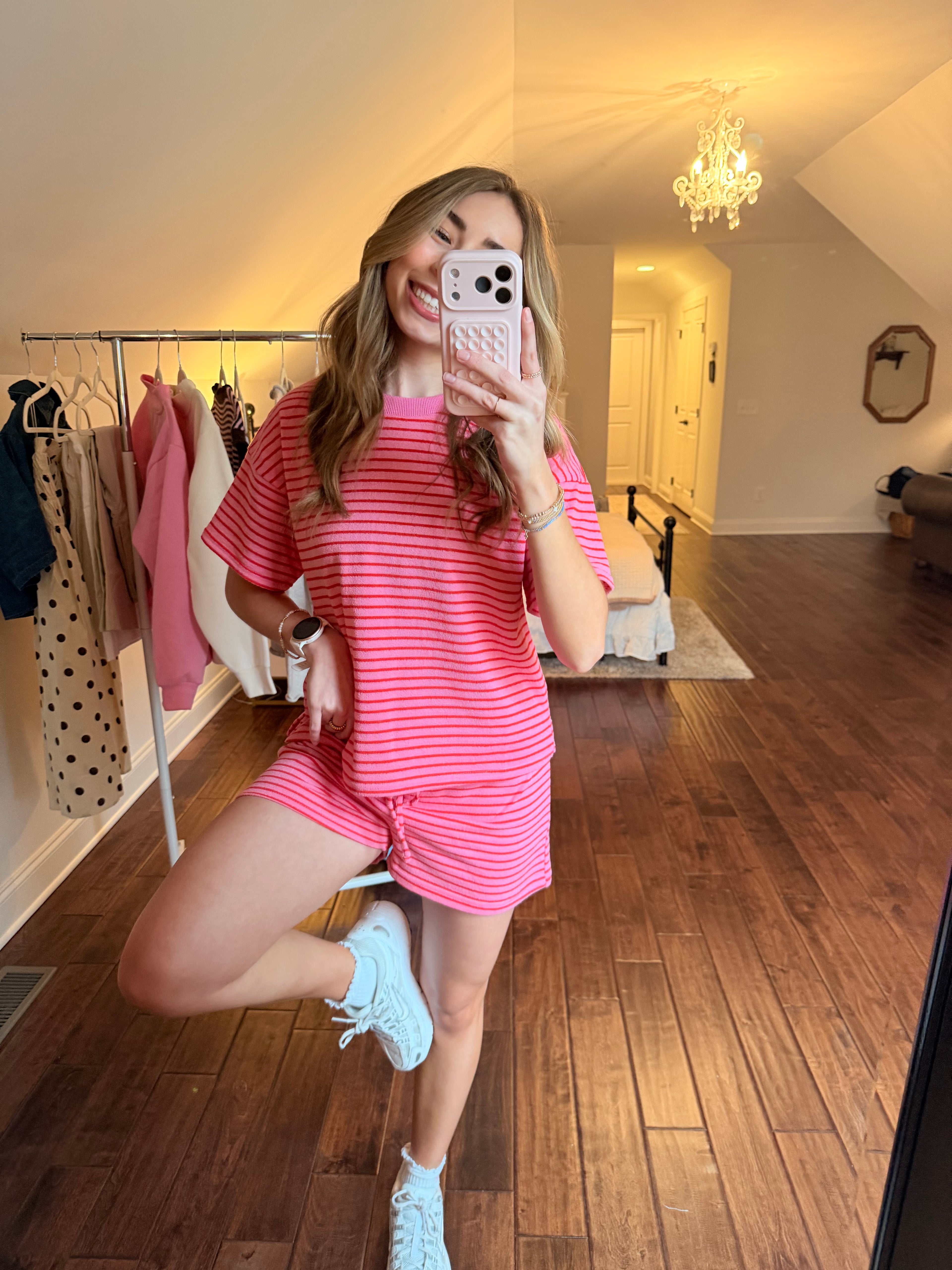 Person taking a mirror selfie wearing a pink matching set in a room with wooden floor and white walls.