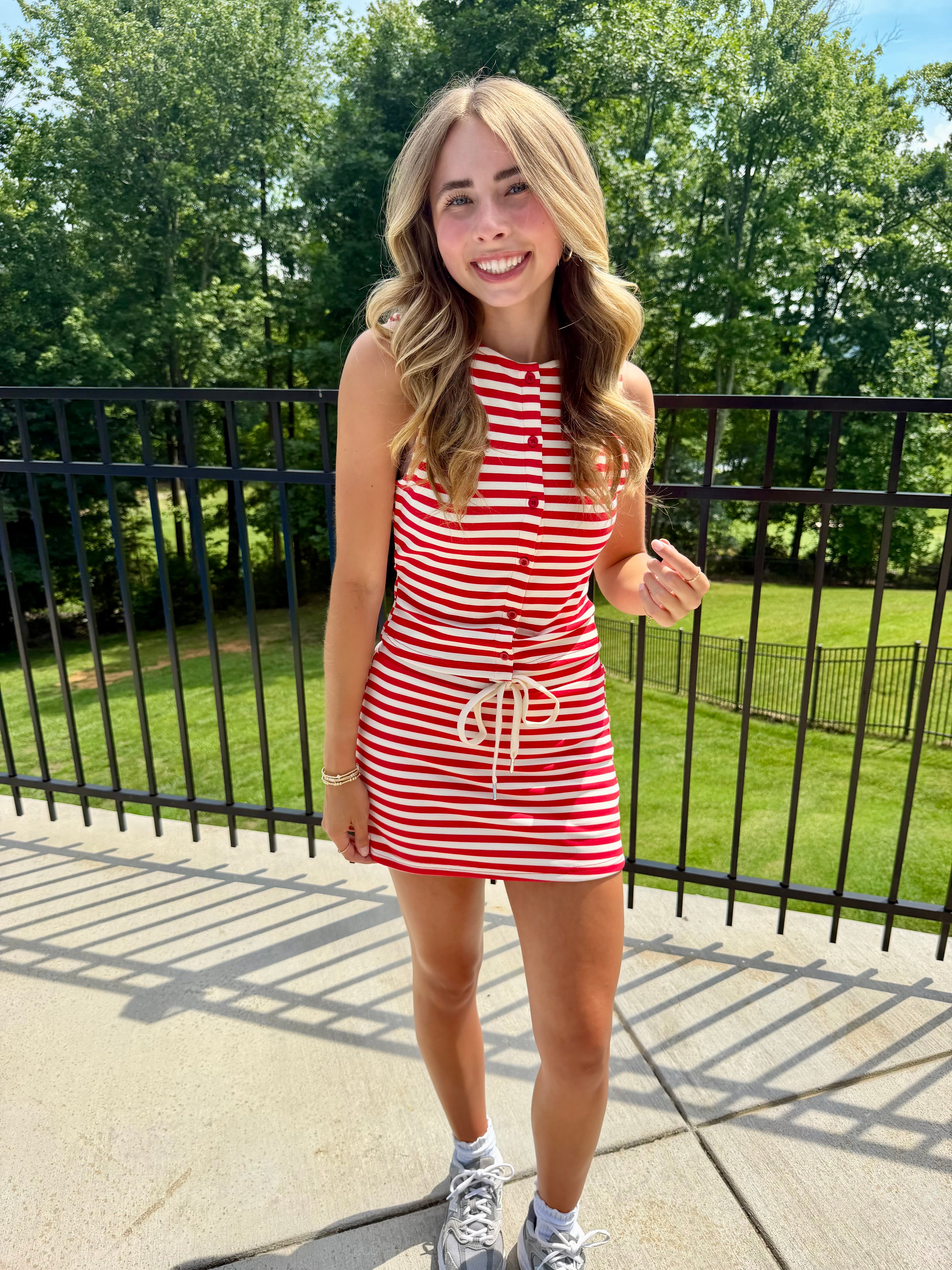 Woman in a red and white striped dress standing outdoors with greenery in the background