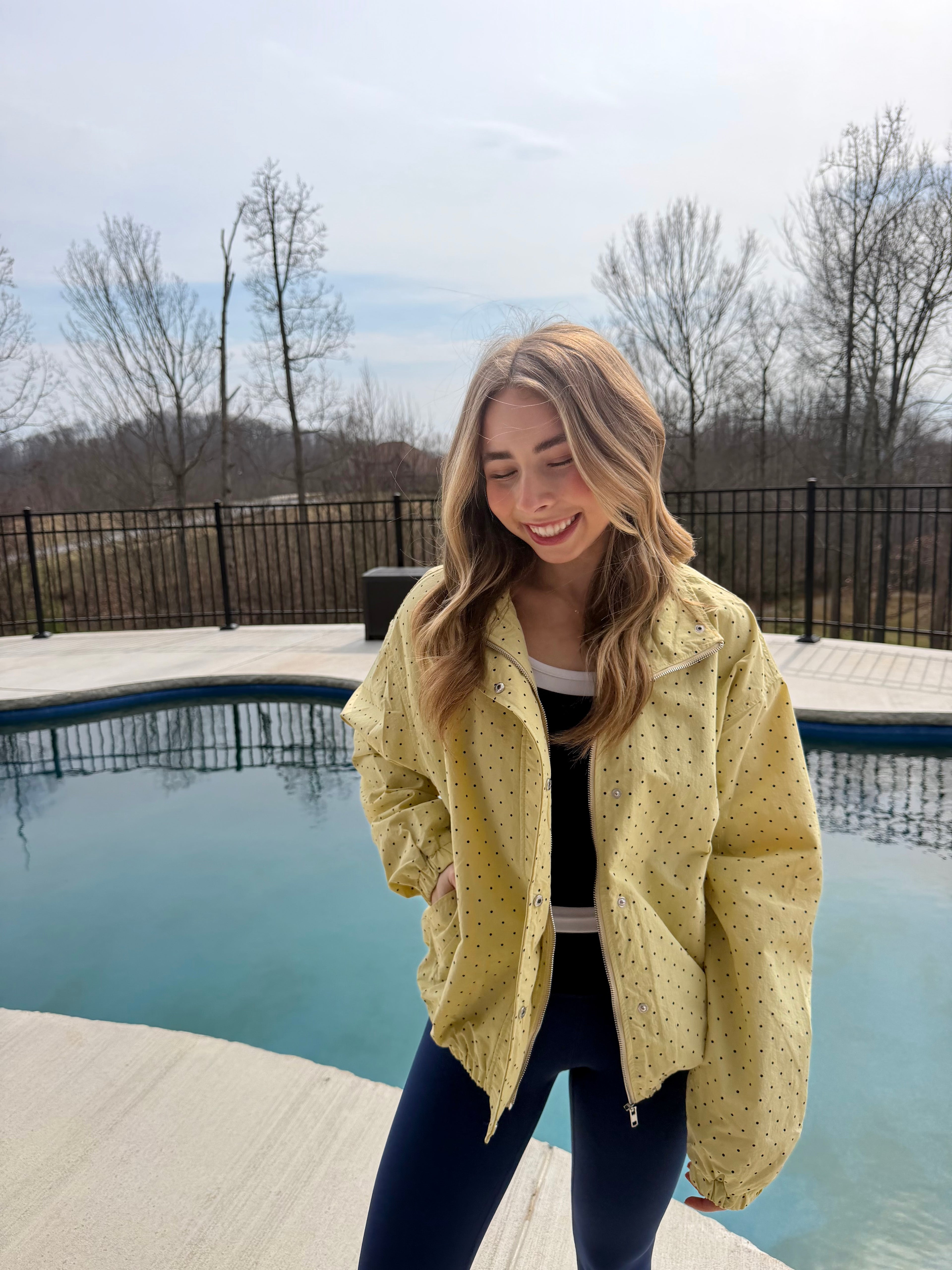 Woman in a yellow jacket standing by a pool with bare trees in the background